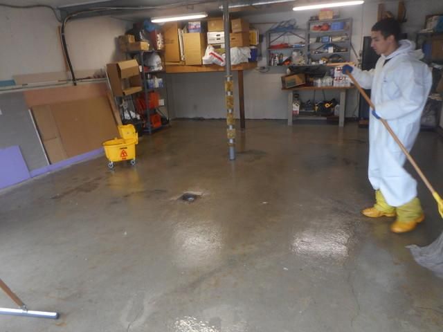 a man in a white suit is cleaning a garage floor with a mop