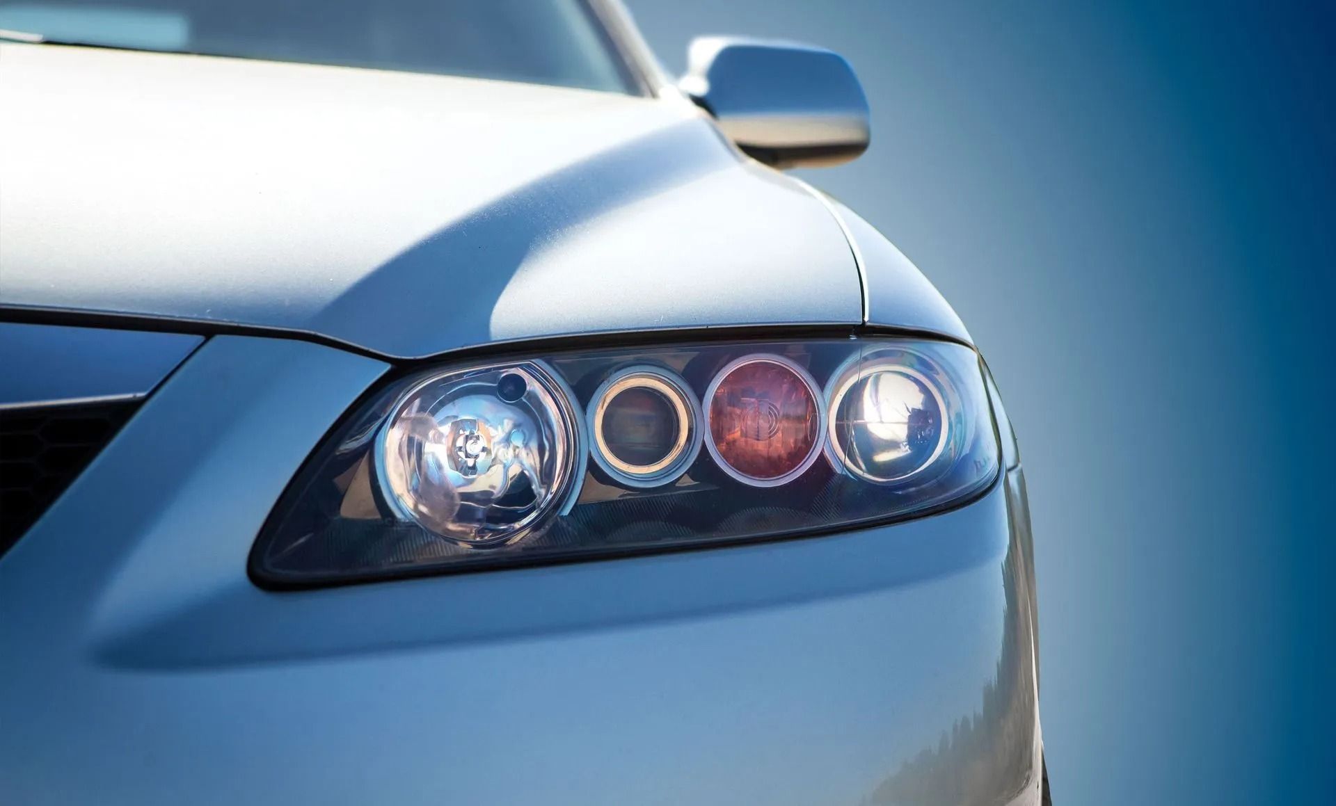 Close-up of a silver car's headlight assembly with multiple circular lights against a blue gradient.