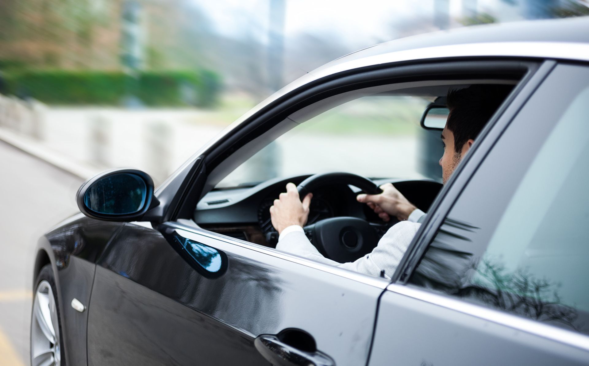 Man driving a black car, hands on the steering wheel, on a road.