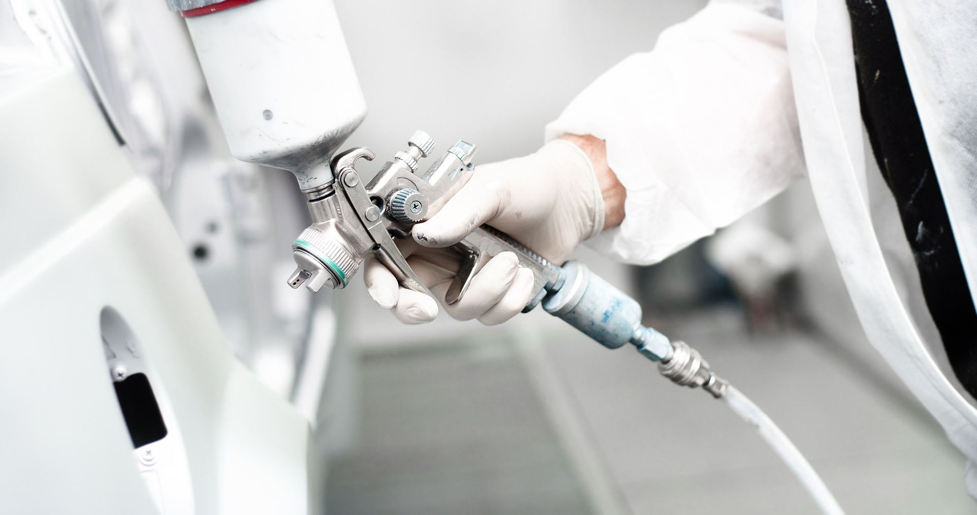 Person wearing protective gear spray-painting a car with a paint gun.