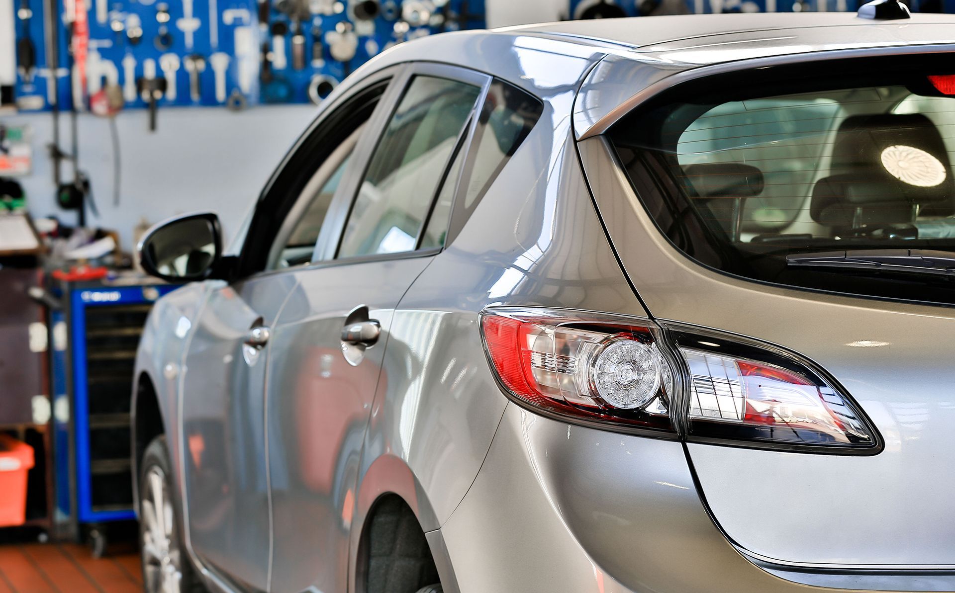Silver hatchback car in a garage with tools in the background.