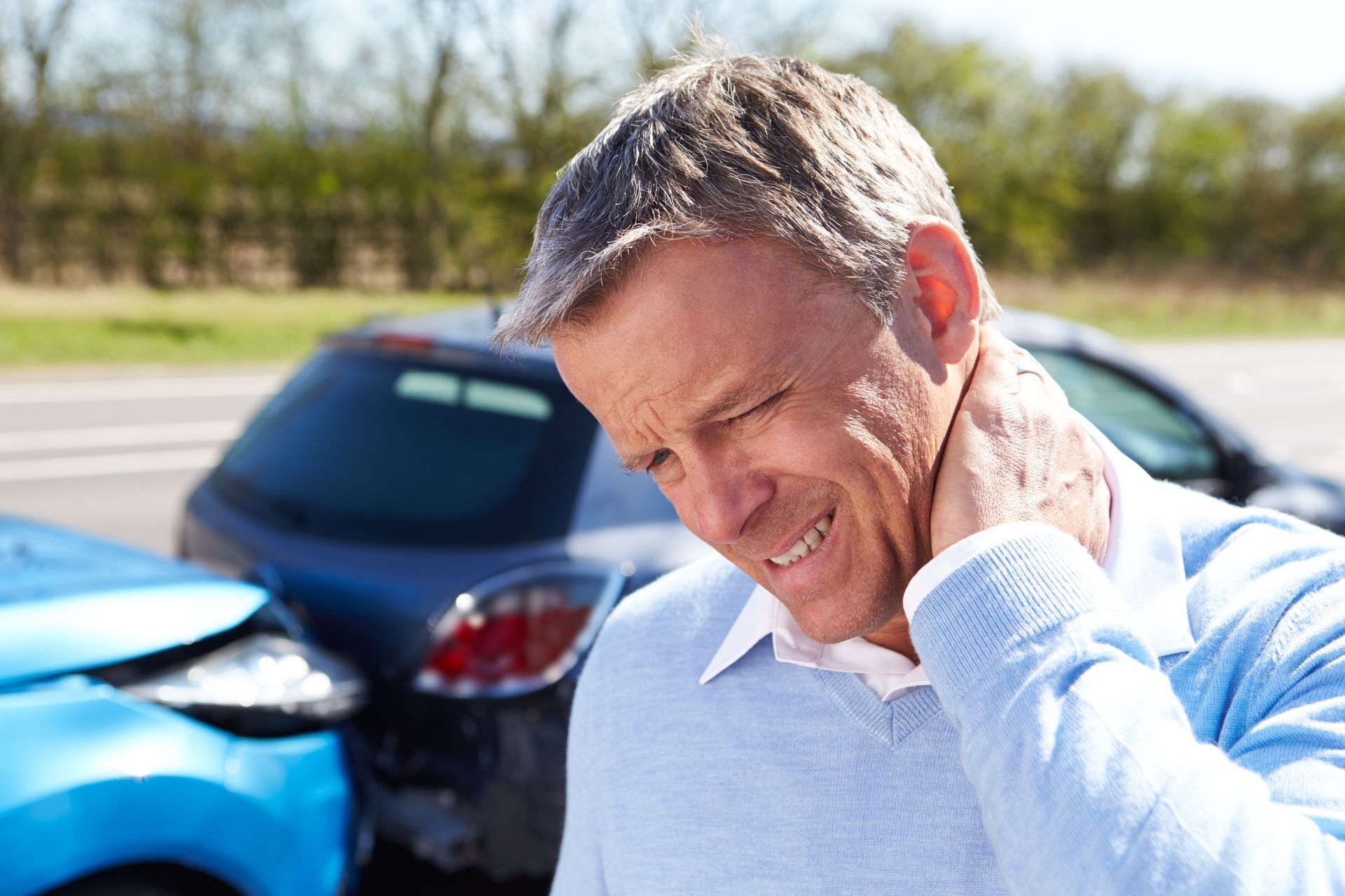 Man holding neck in pain after a car accident. Cars with damage in the background.