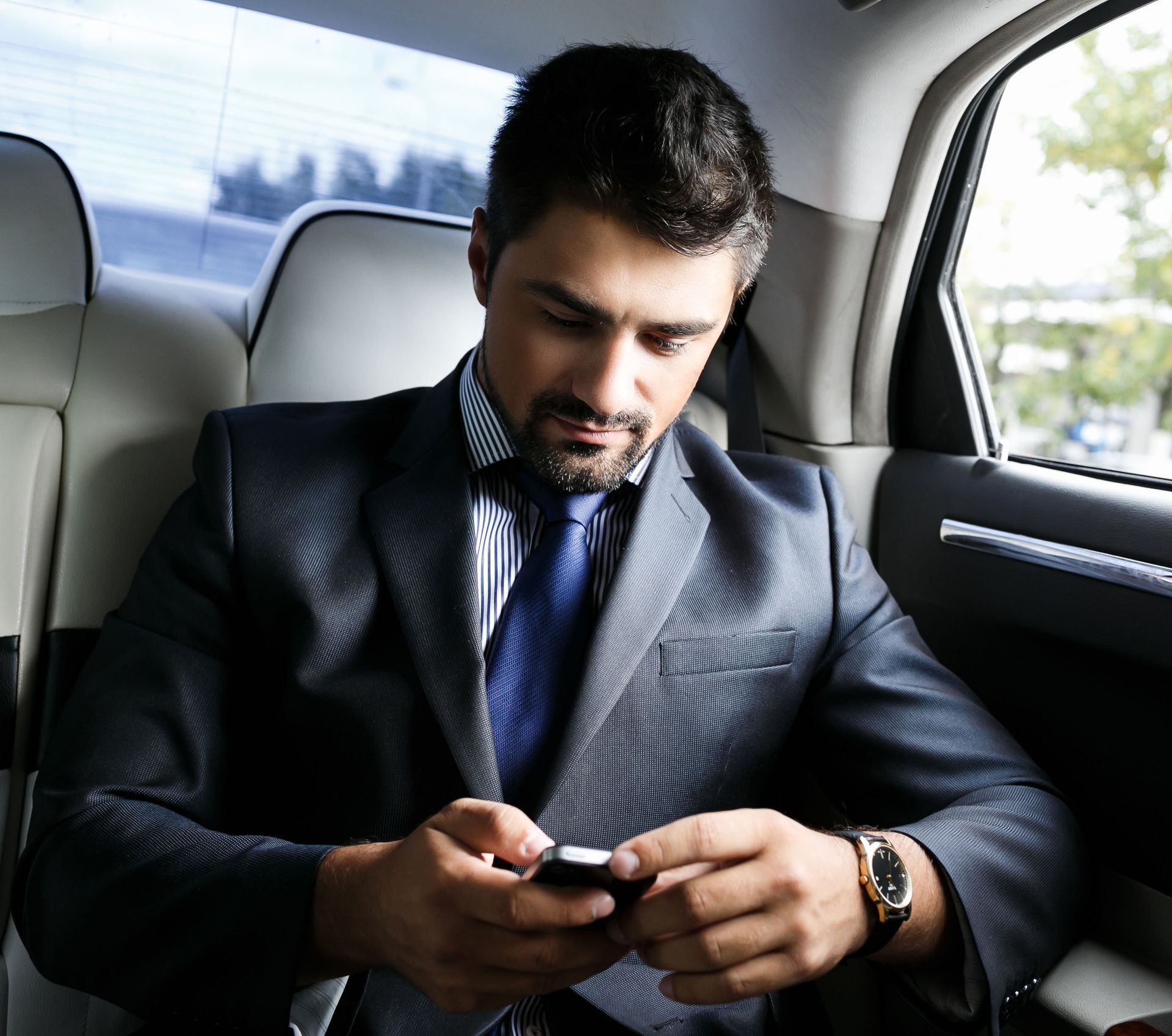 Man in suit looks at his phone while seated in a car.