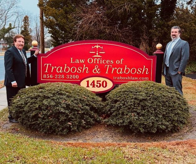 Two men in suits stand by a red sign that reads