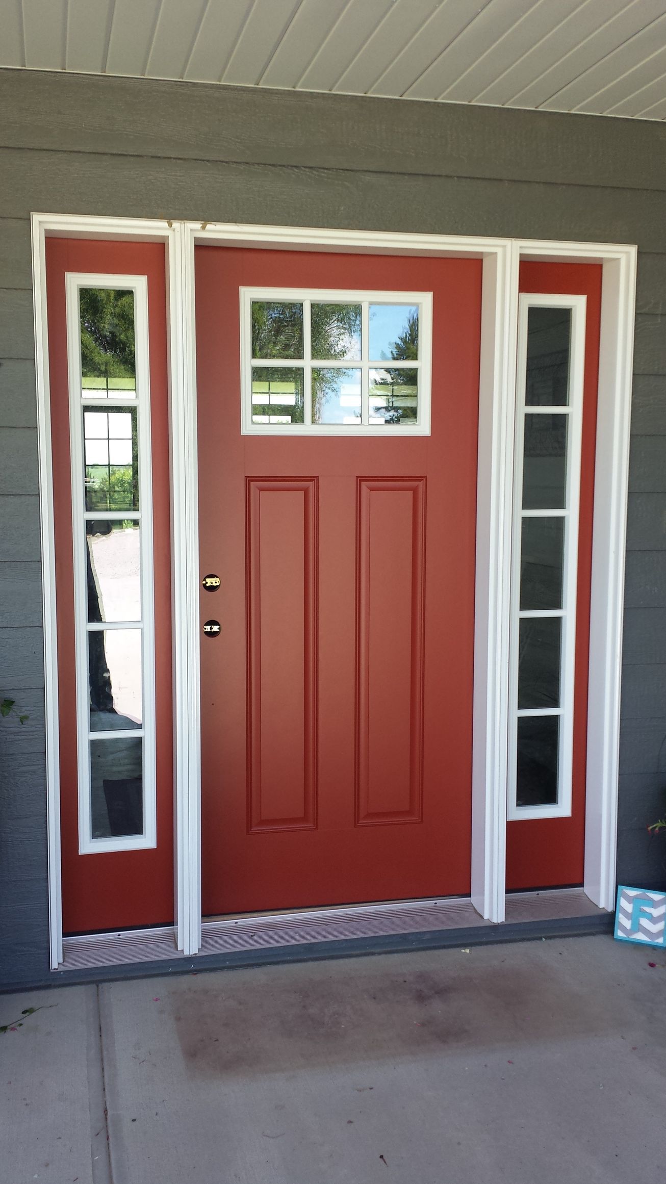 A red door with white trim is on a gray house
