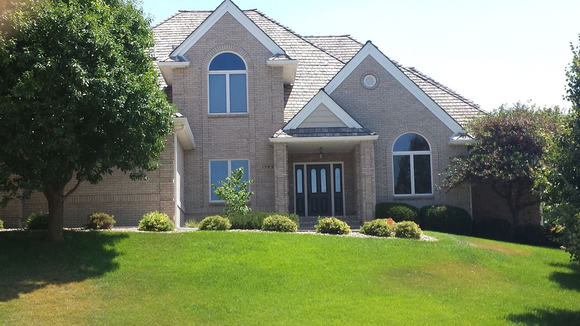 A large brick house sits on a lush green hillside