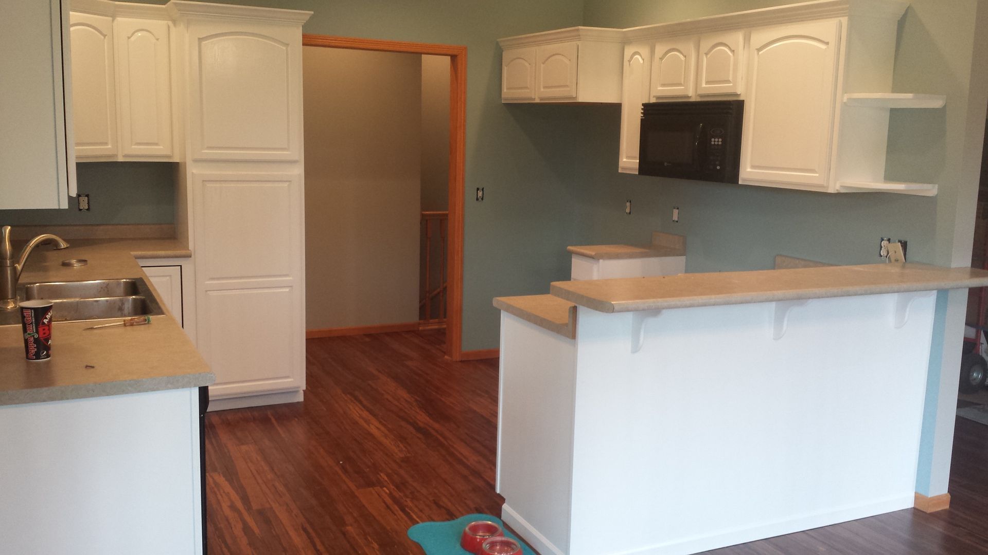 An empty kitchen with white cabinets and hardwood floors.