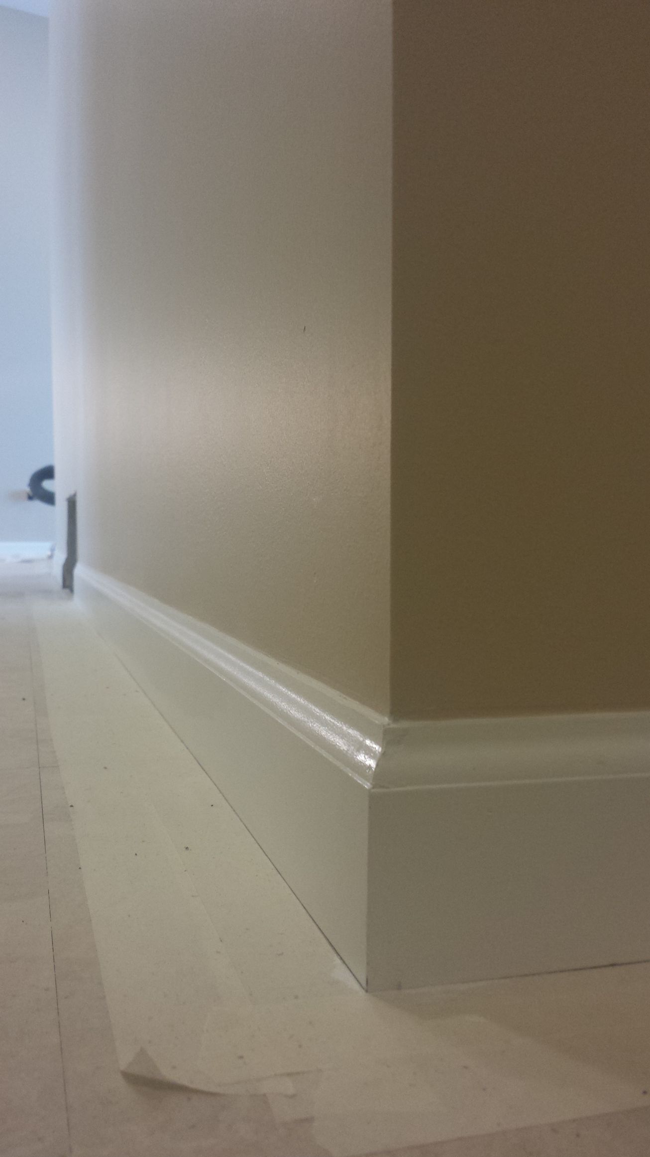 A corner of a room with a white baseboard and beige walls.