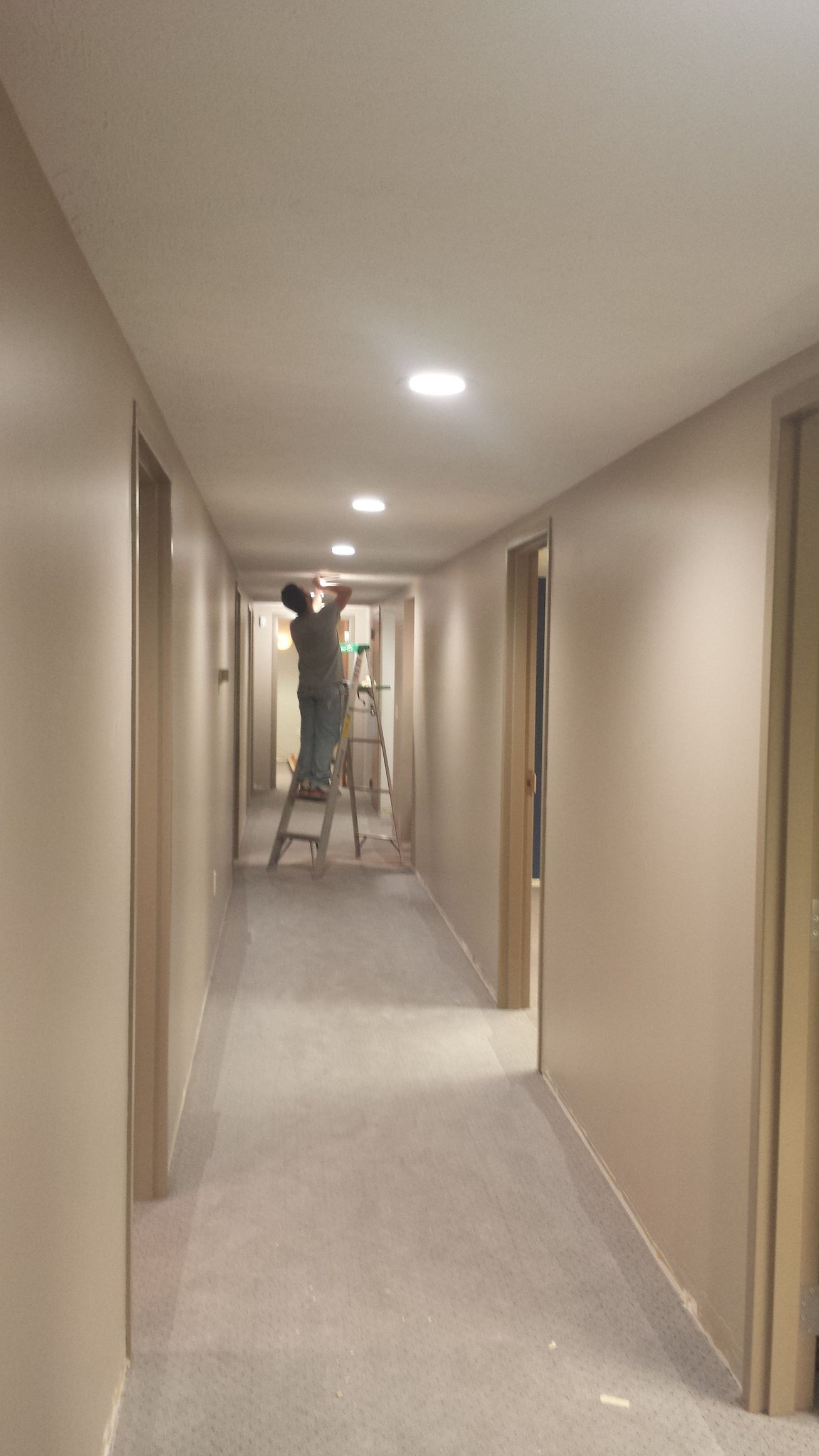 A man is standing on a ladder in a long hallway.