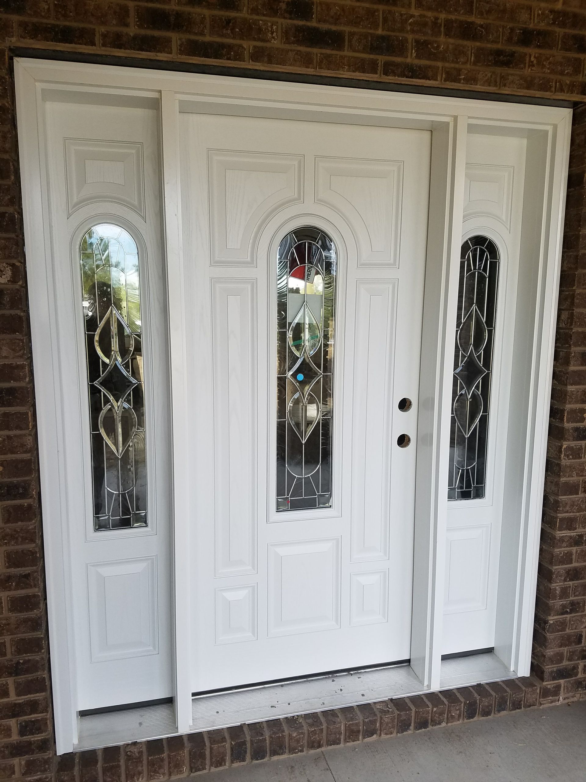 A white door with stained glass windows is on a brick wall.