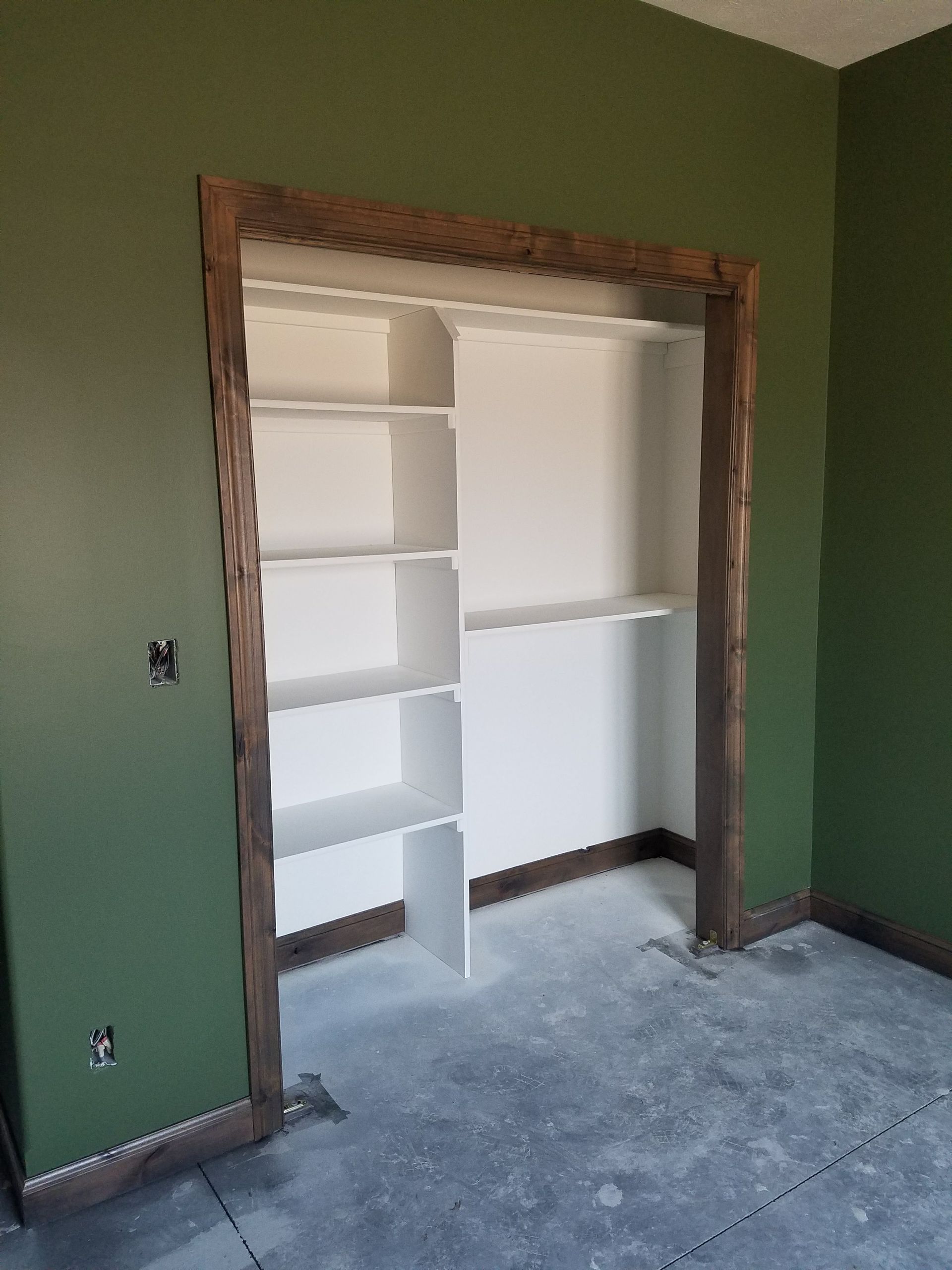 A closet with green walls and white shelves in a room.