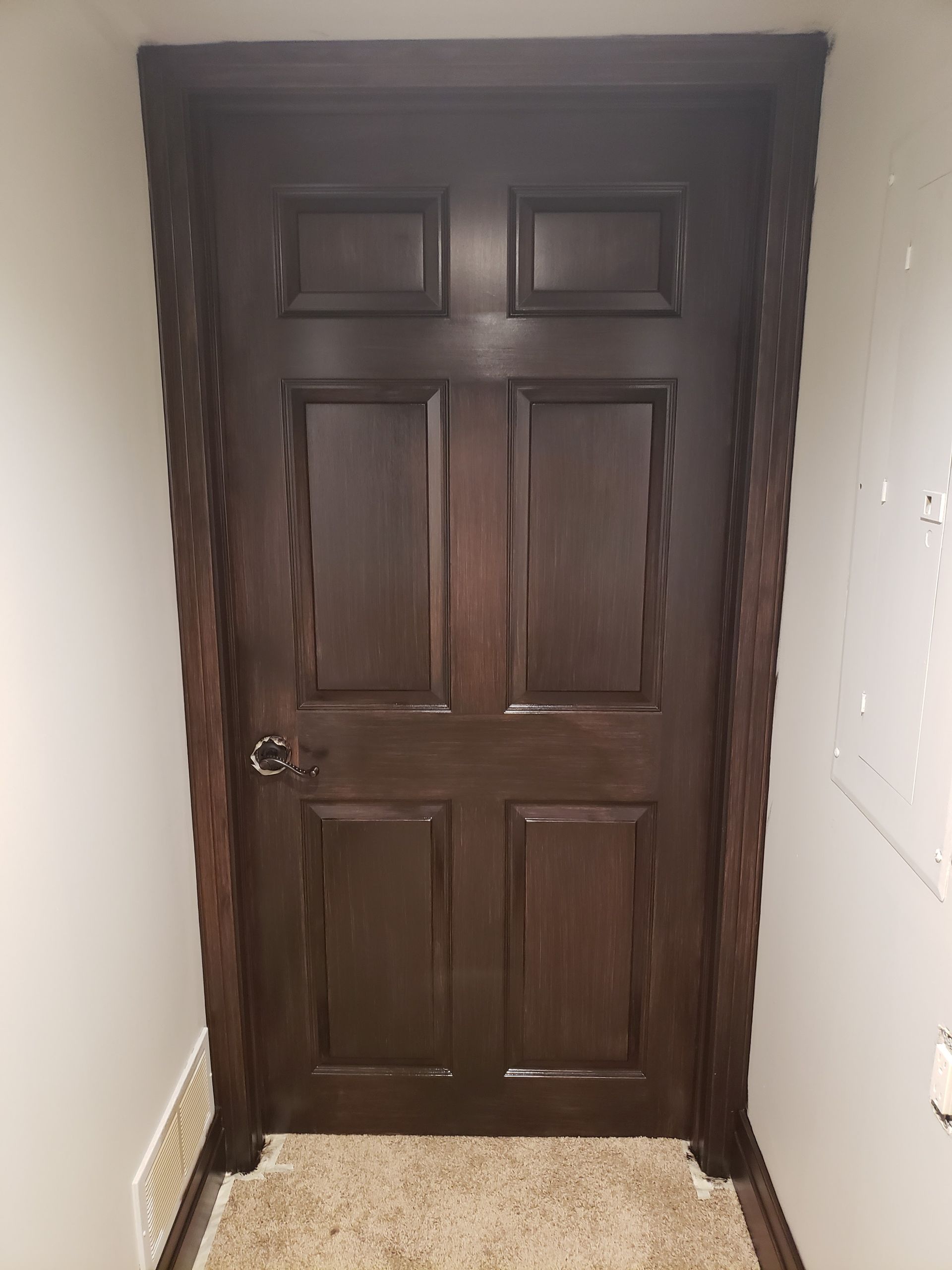 A dark wooden door is sitting in a hallway next to a wall.