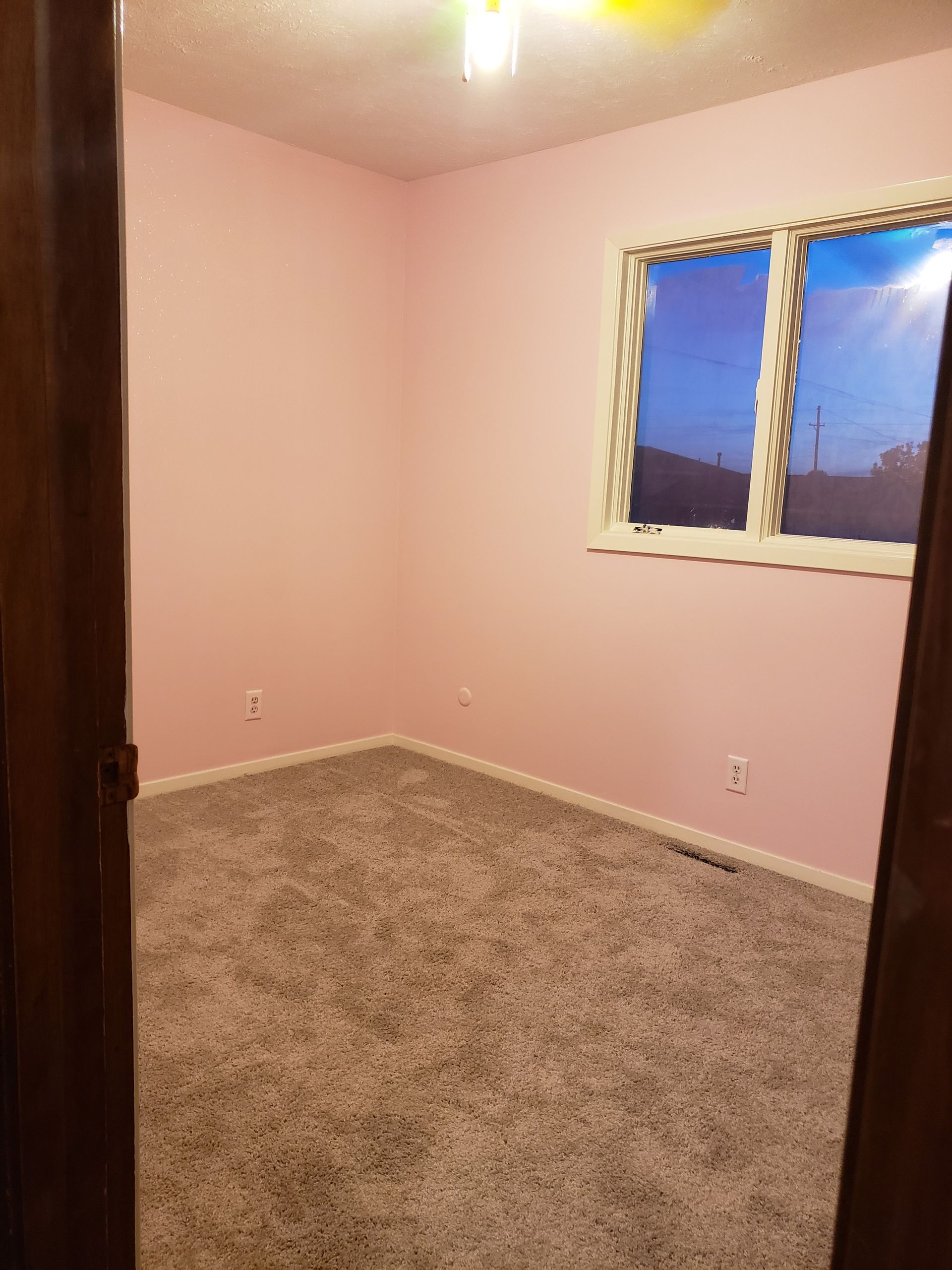 A bedroom with pink walls and a window.