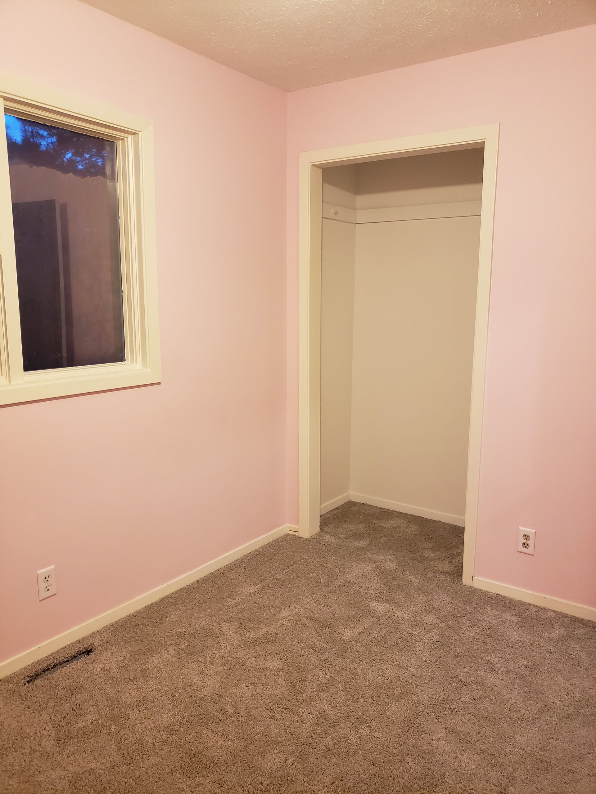 An empty room with pink walls and a window.