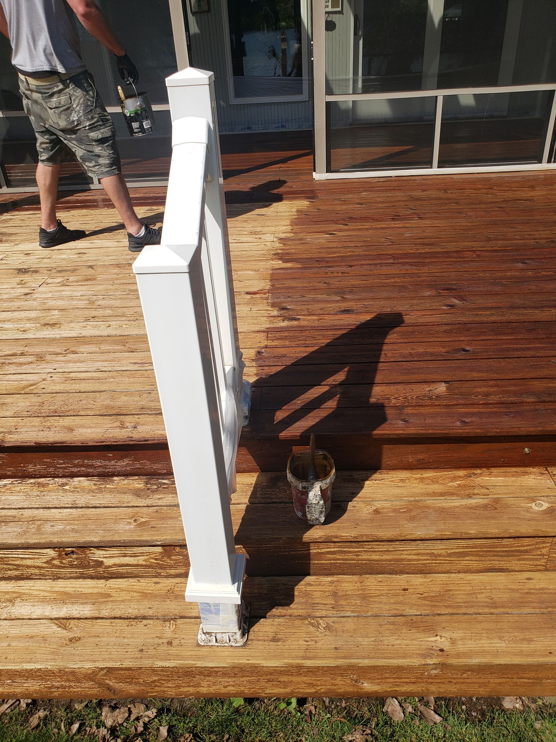 A man is painting a wooden deck with a white railing.