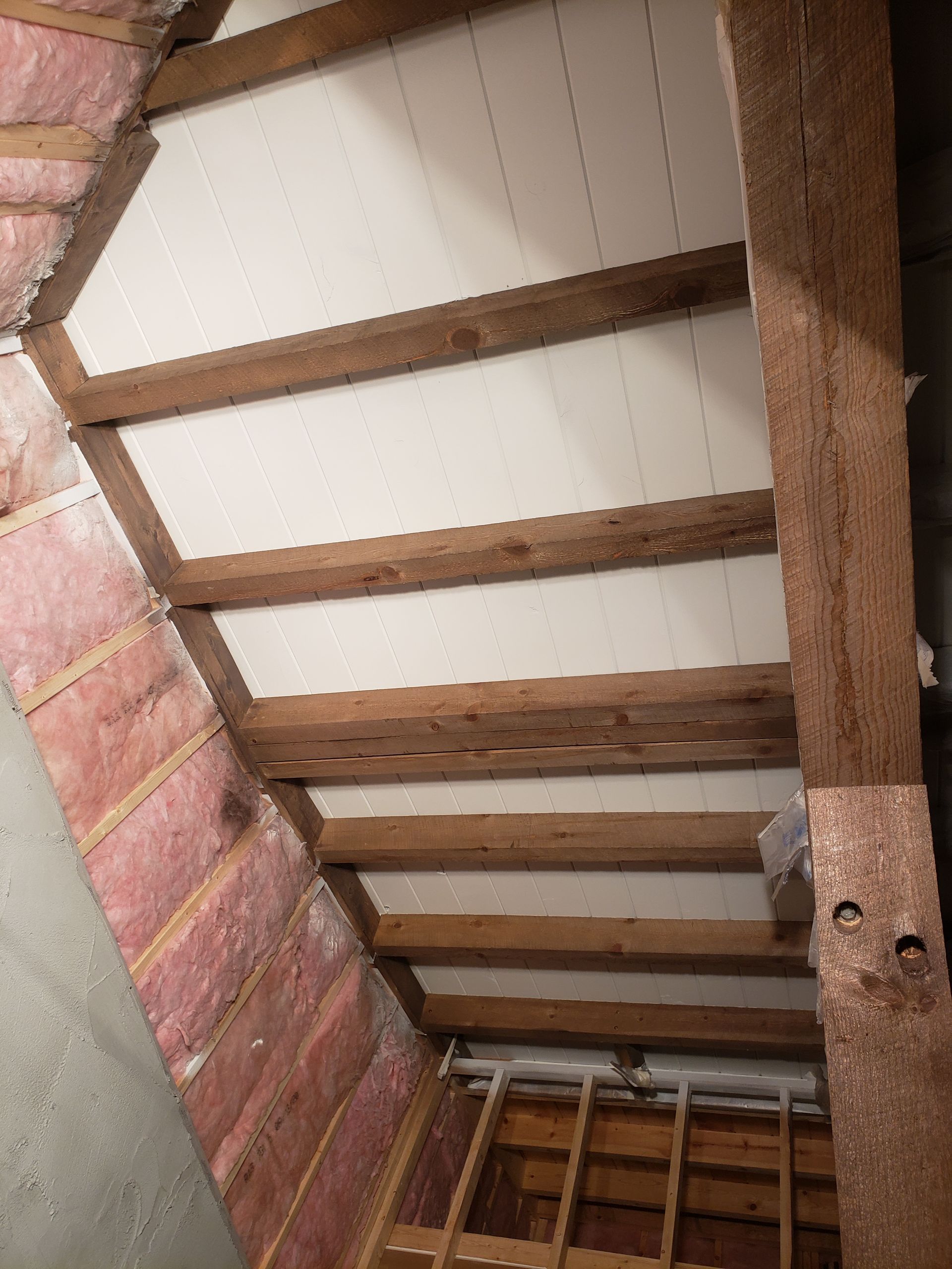 A ceiling with wooden beams and styrofoam insulation