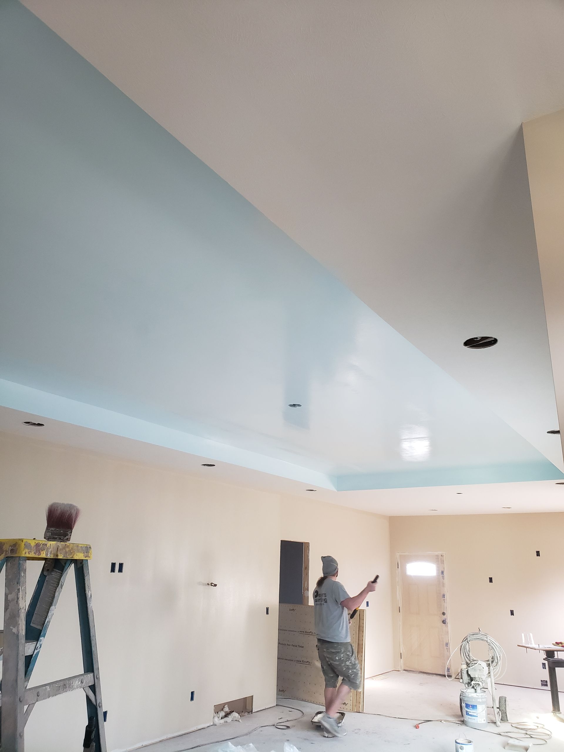 A man is standing in a room painting the ceiling.