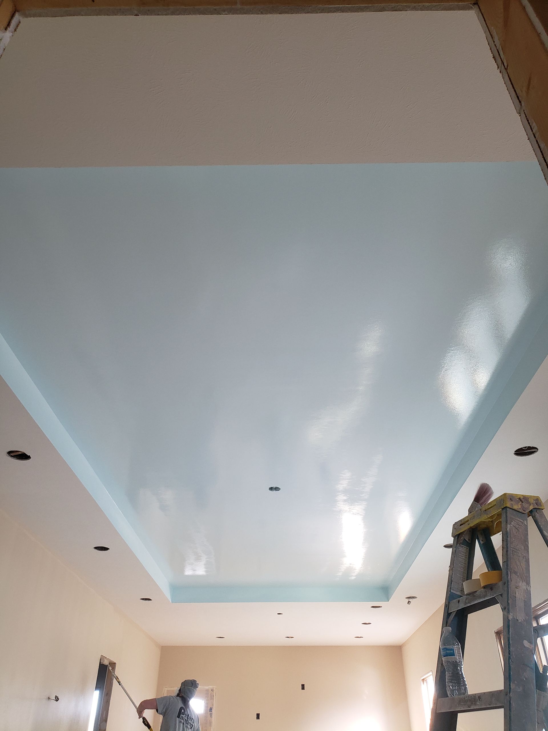 A man is standing on a ladder painting the ceiling of a room.