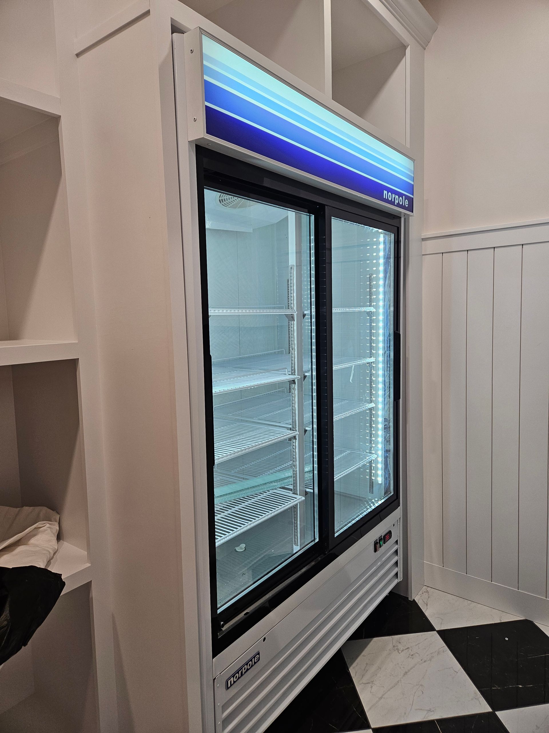 A refrigerator with sliding glass doors is in a room with a checkered floor.