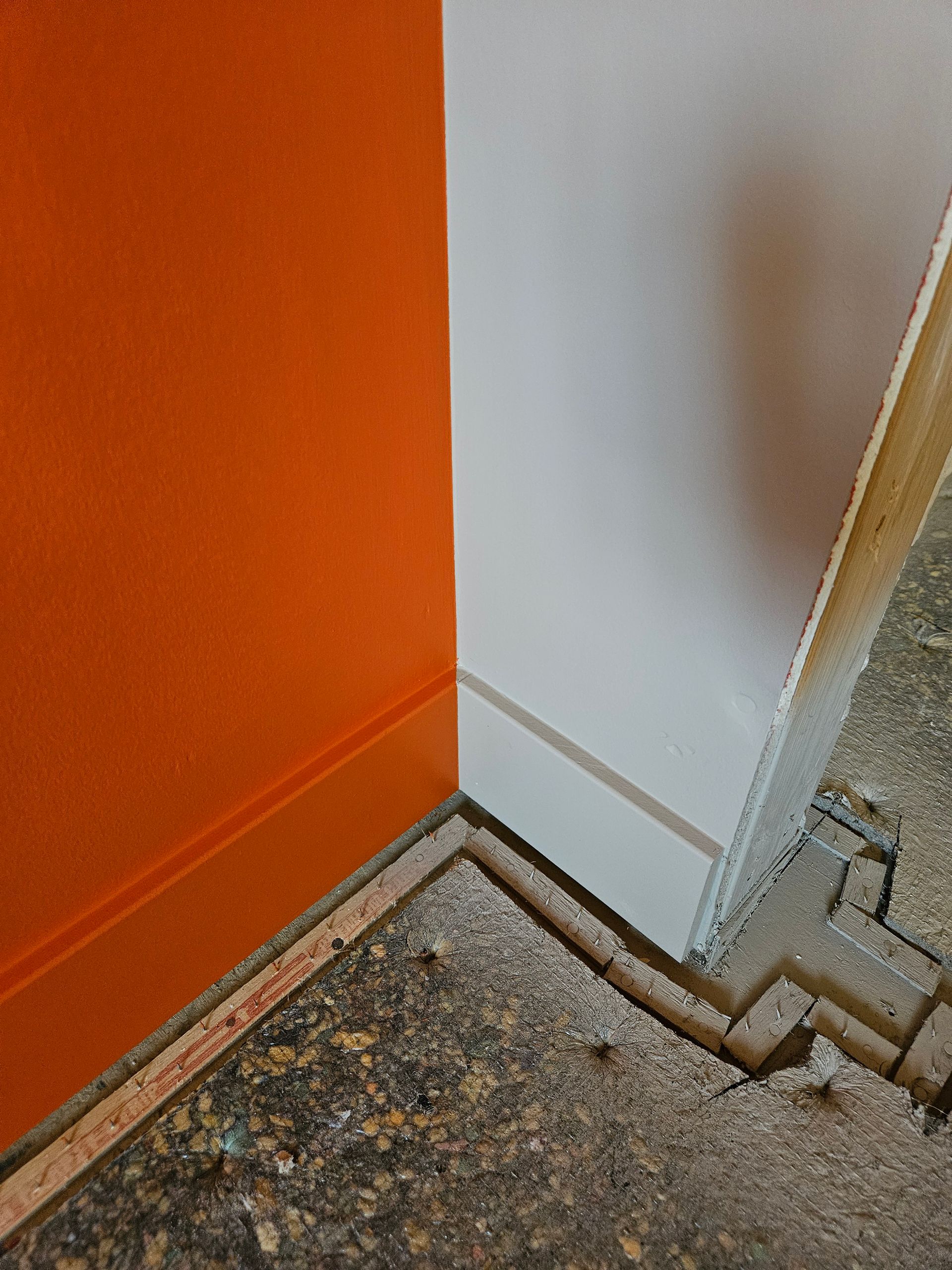 A corner of a room with an orange wall and a white wall.