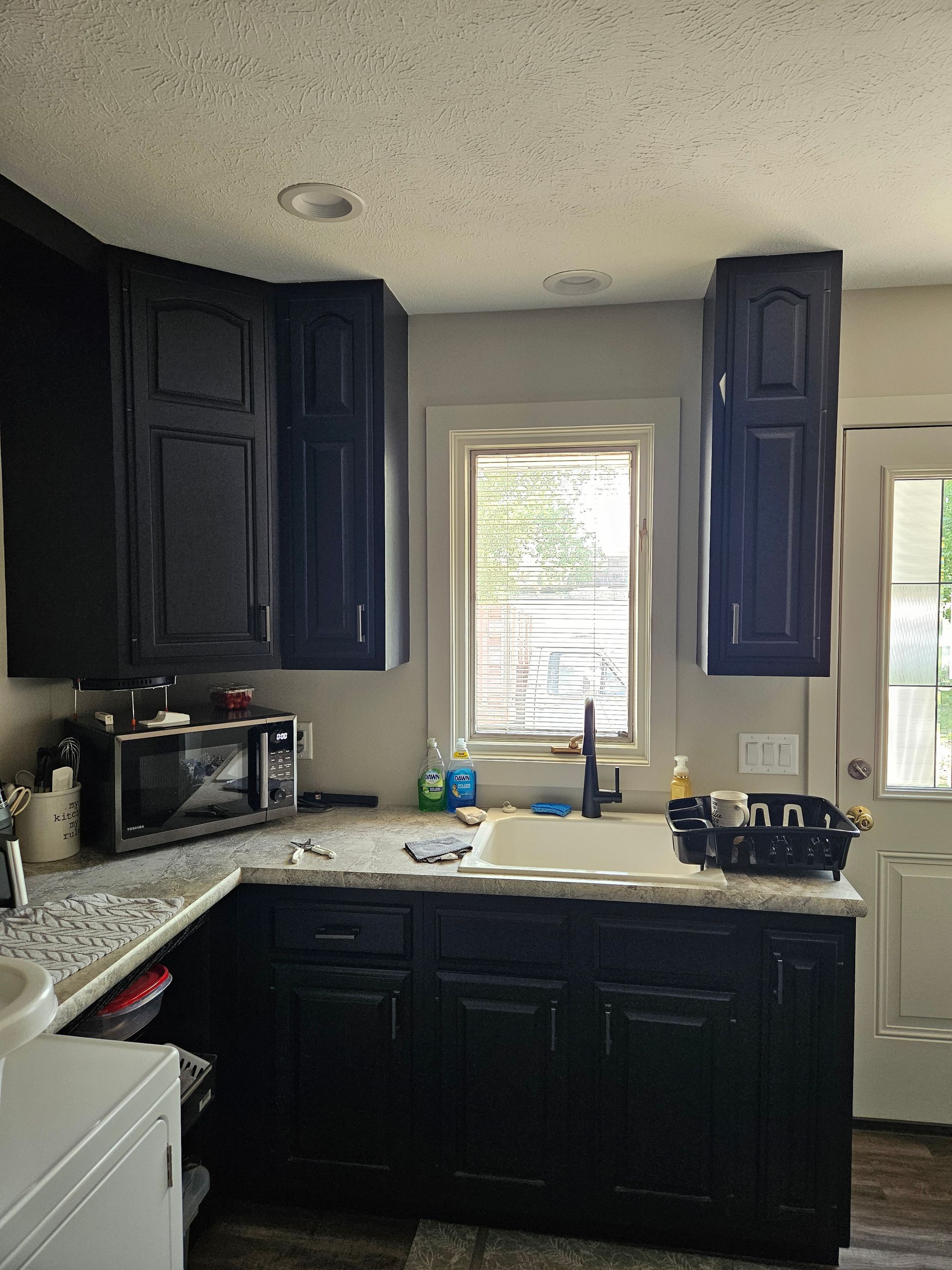 A kitchen with black cabinets , a sink , a microwave , and a window.