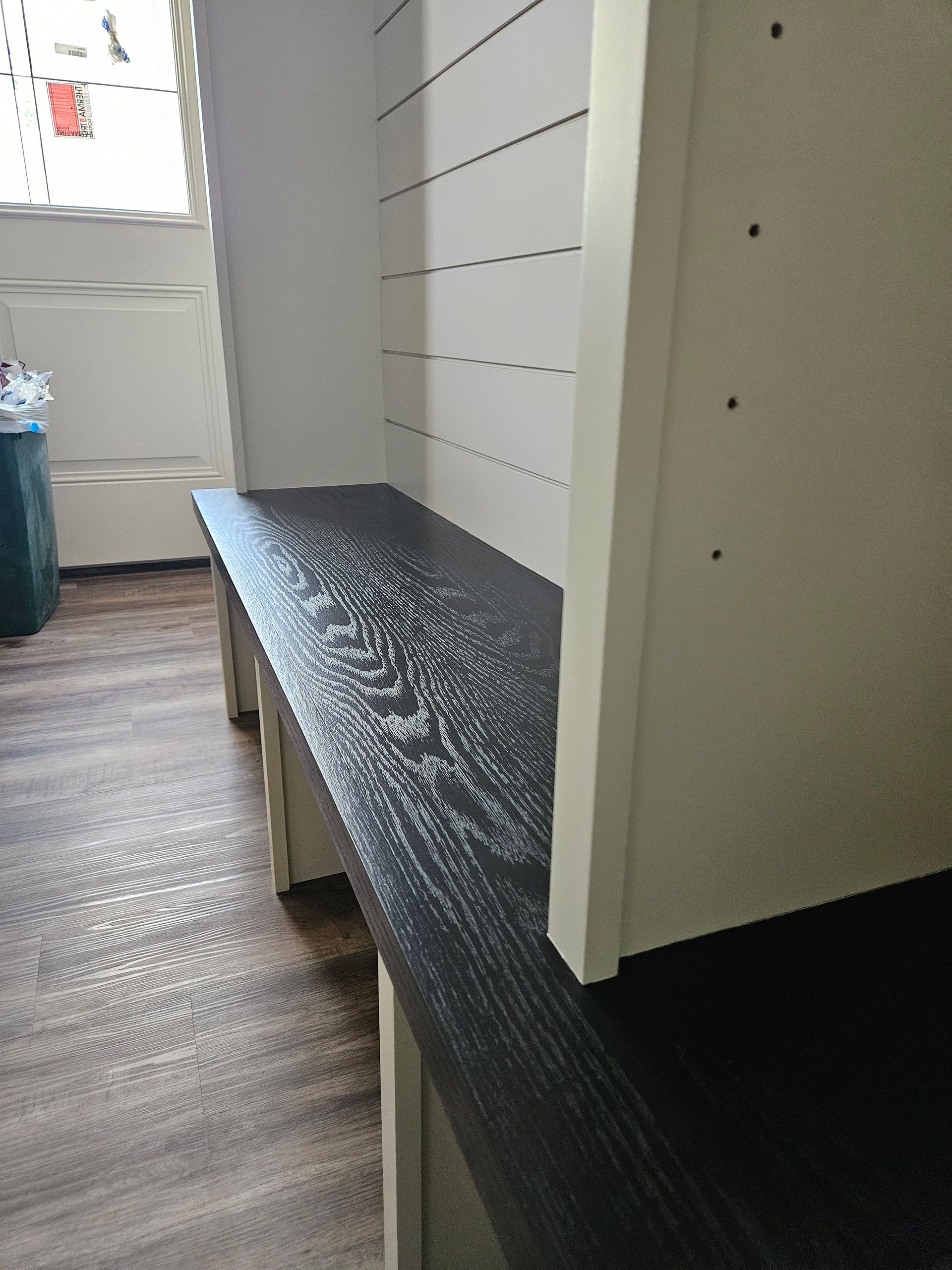 A white shelf with a black top is in a room next to a window.