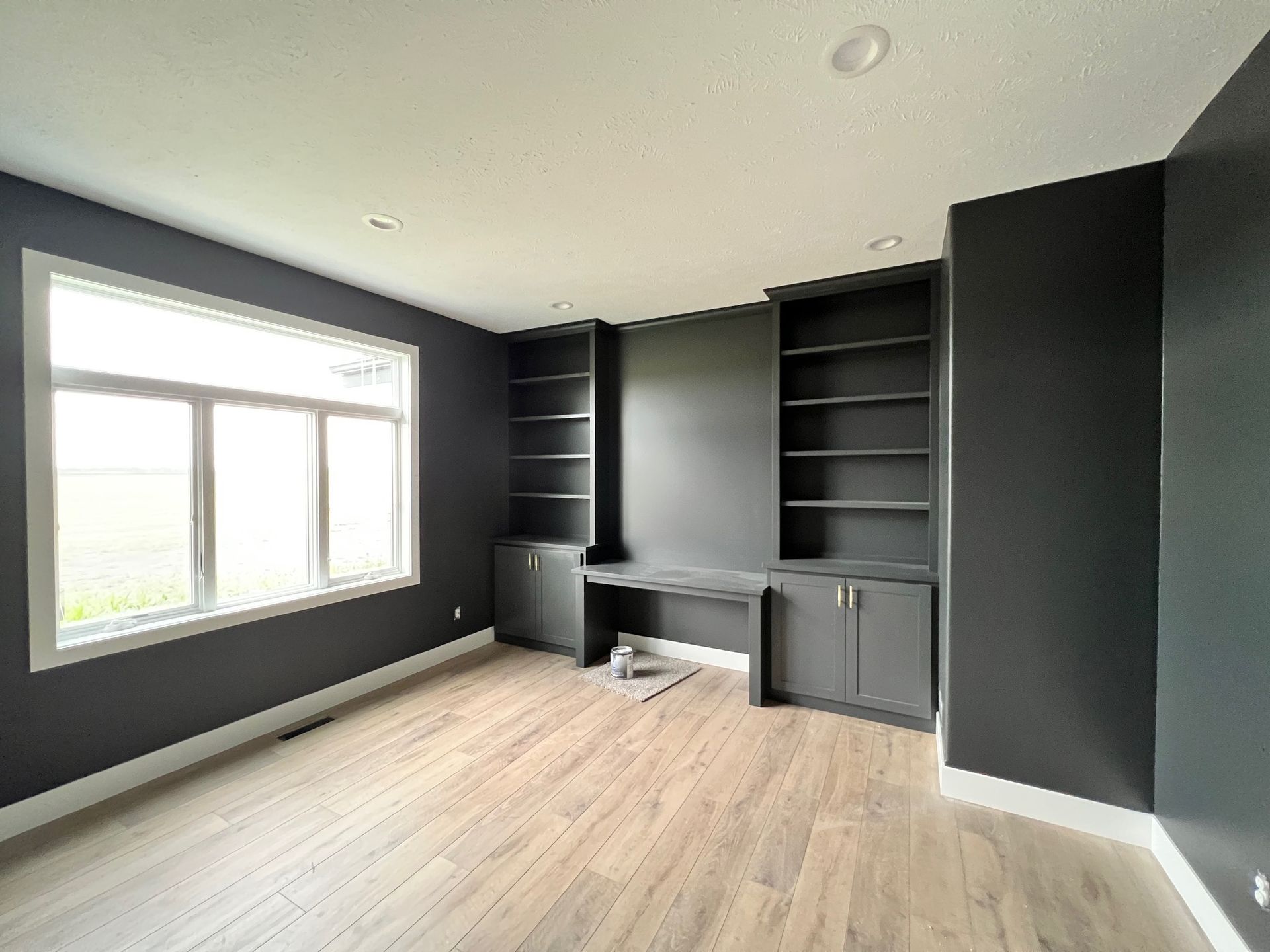 An empty room with black walls and wooden floors has a desk and shelves.