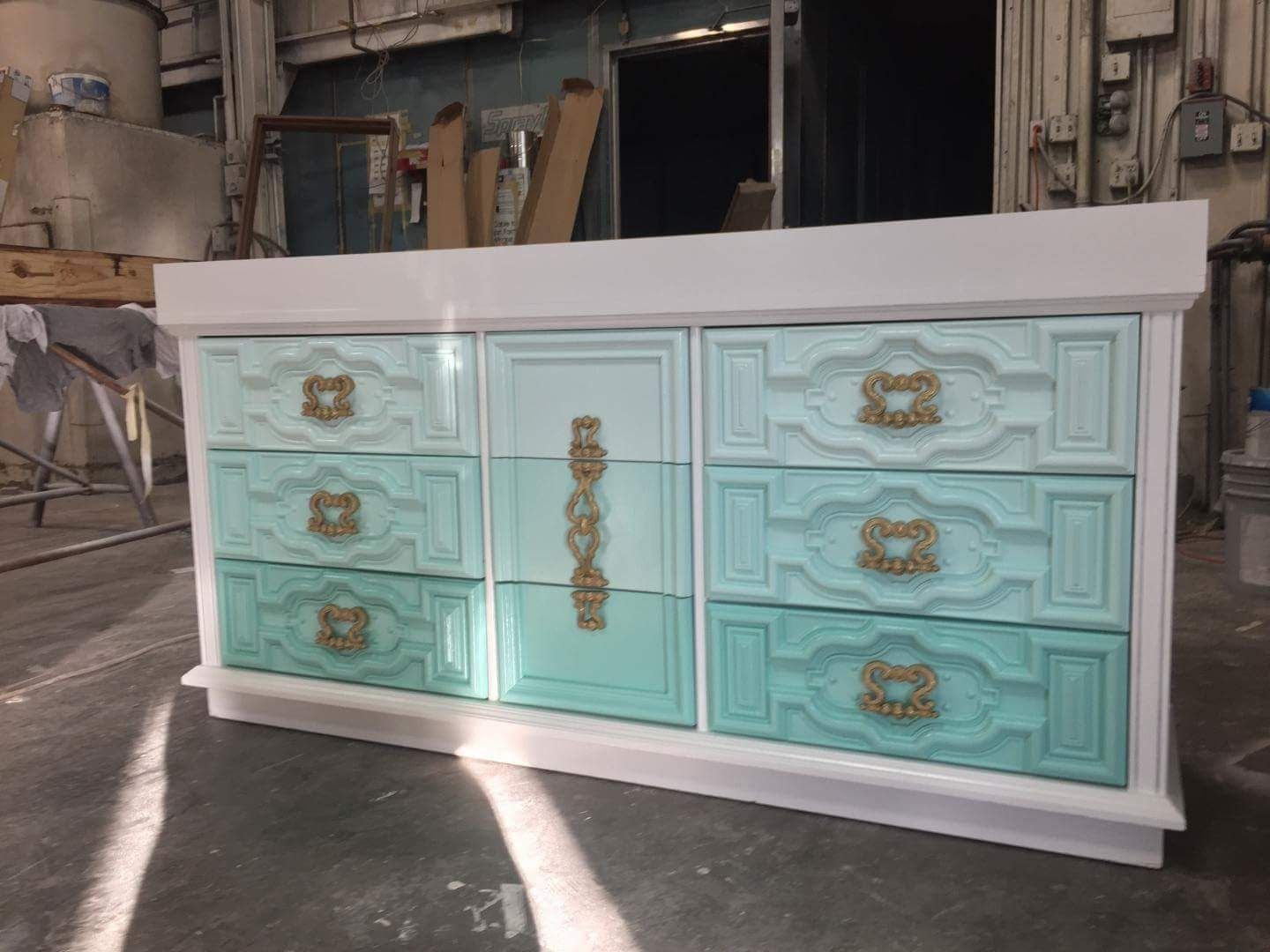 A blue and white dresser with gold handles is sitting on a table.