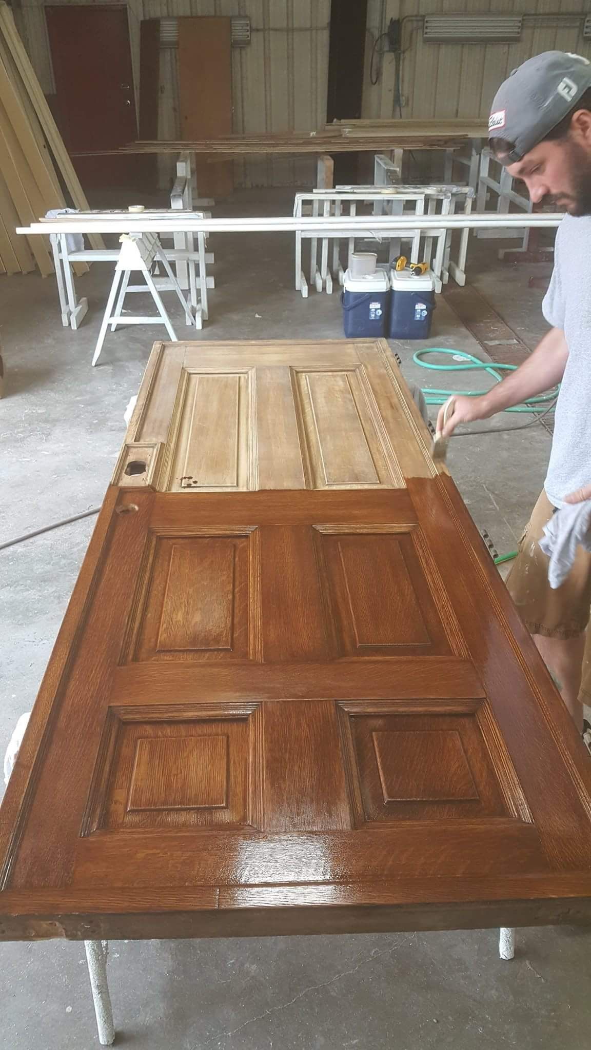A man is painting a wooden door in a workshop.