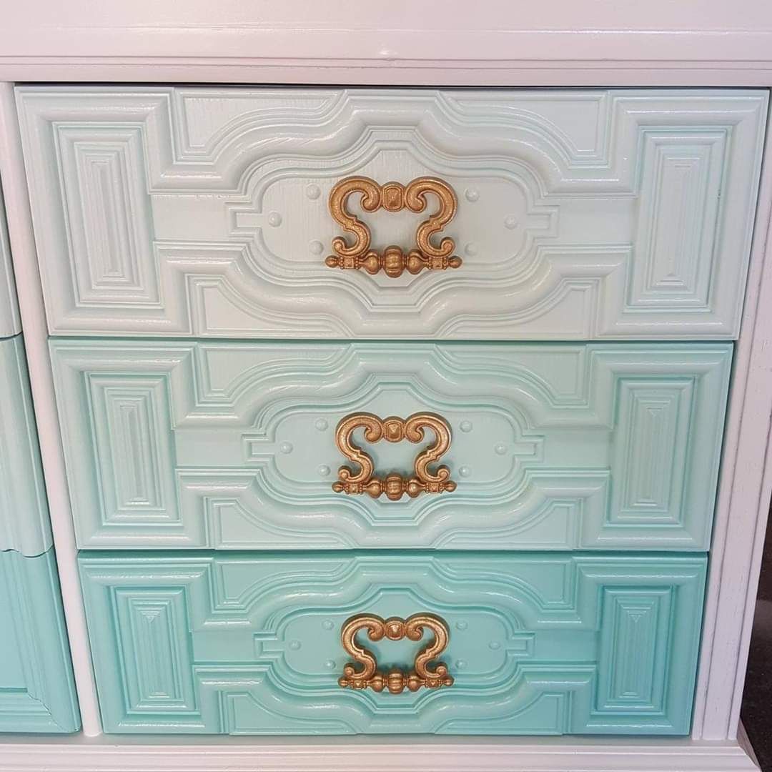 A dresser with three drawers painted different colors and gold handles.