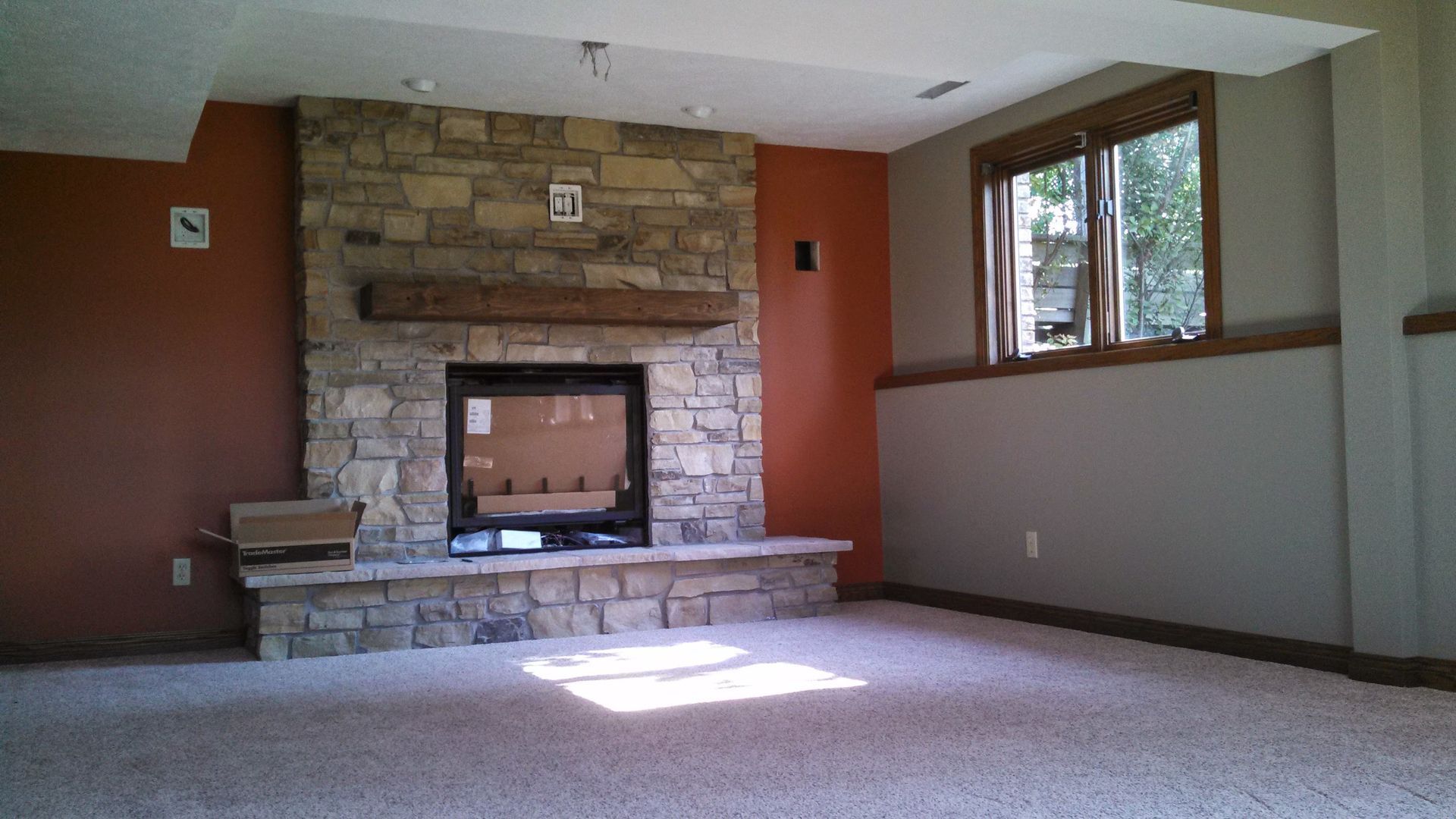 An empty living room with a stone fireplace and a window