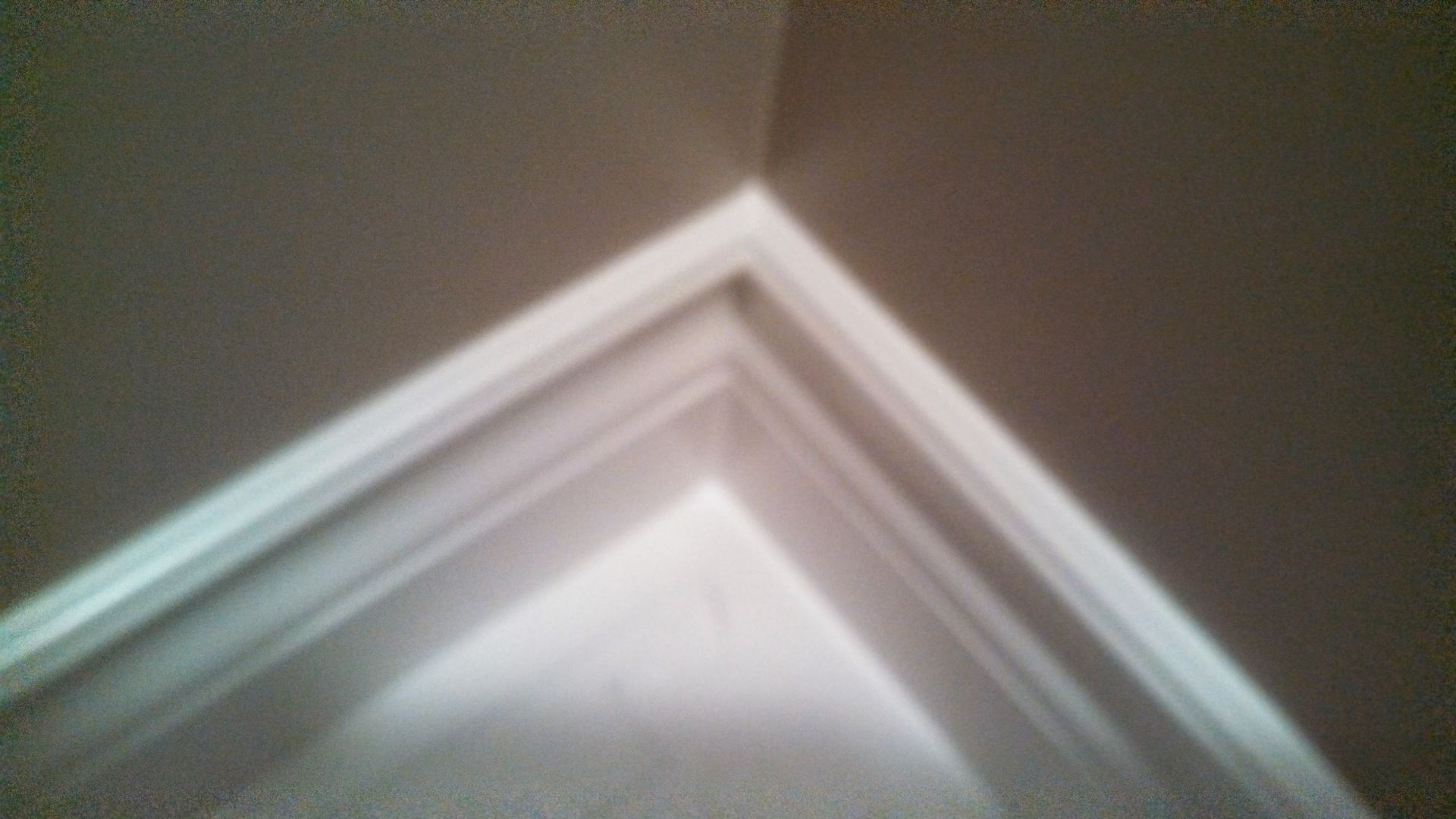A corner of a room with white molding and a shadow on the wall.