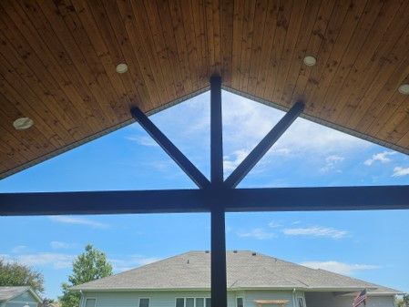 A screened in porch with a wooden ceiling and a view of a house.