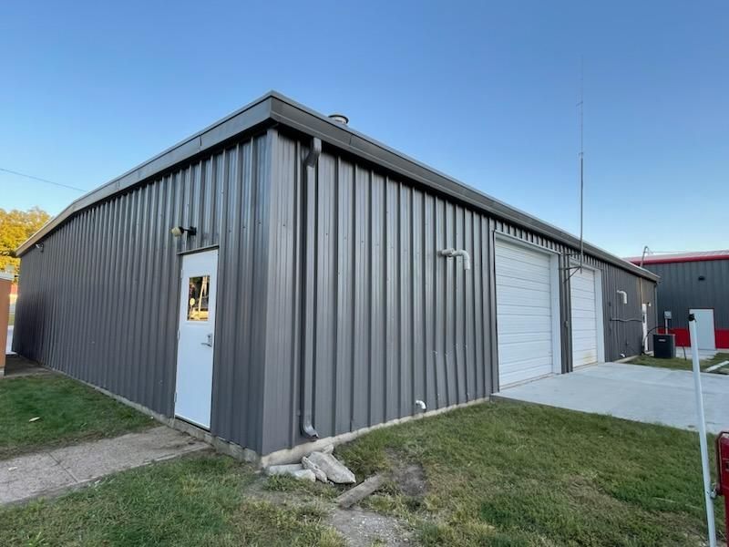 A large gray metal building with a white door and two garage doors