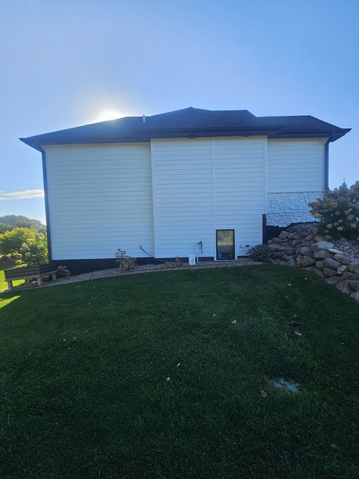 A white house with a black roof is sitting on top of a lush green lawn