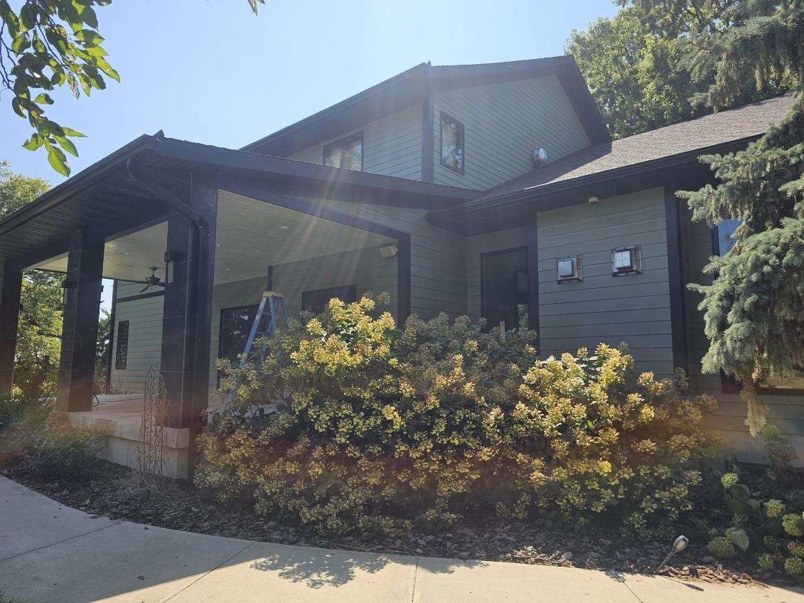A large, newly painted house with a porch and bushes in front of it