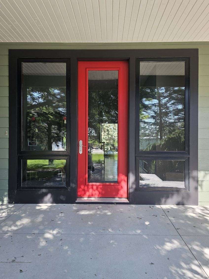 A newly painted front door area of a house with a red door and black windows