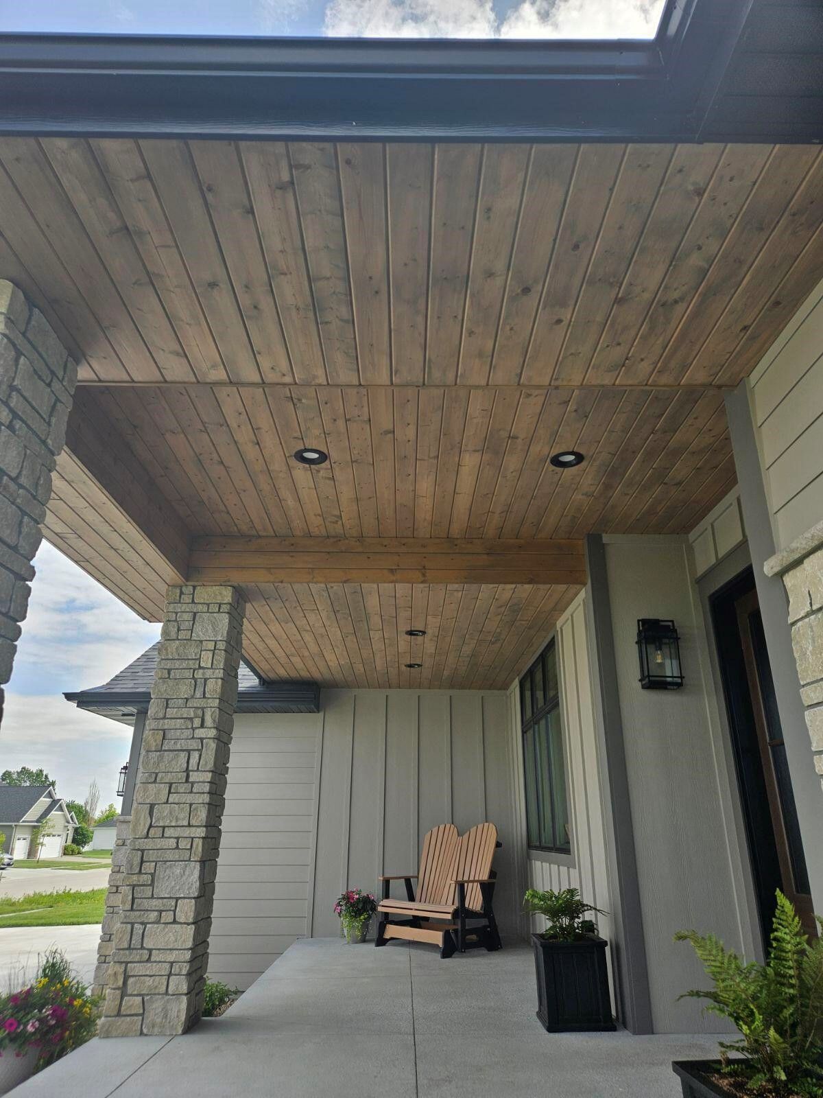 A porch with a wooden ceiling and chairs on it.