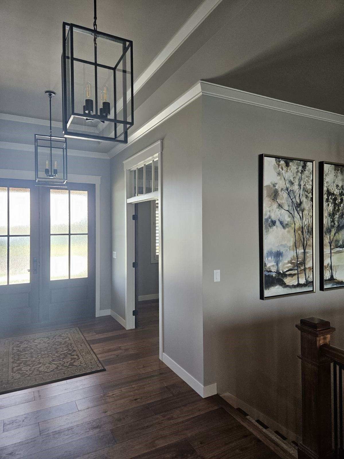 A hallway with hardwood floors , gray walls , and two paintings on the wall.