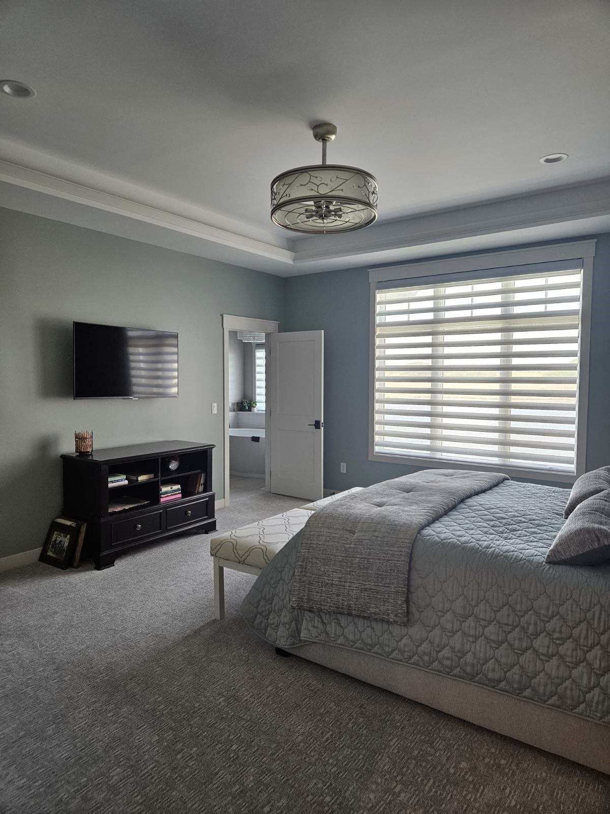 A bedroom with a bed , television , dresser and window.