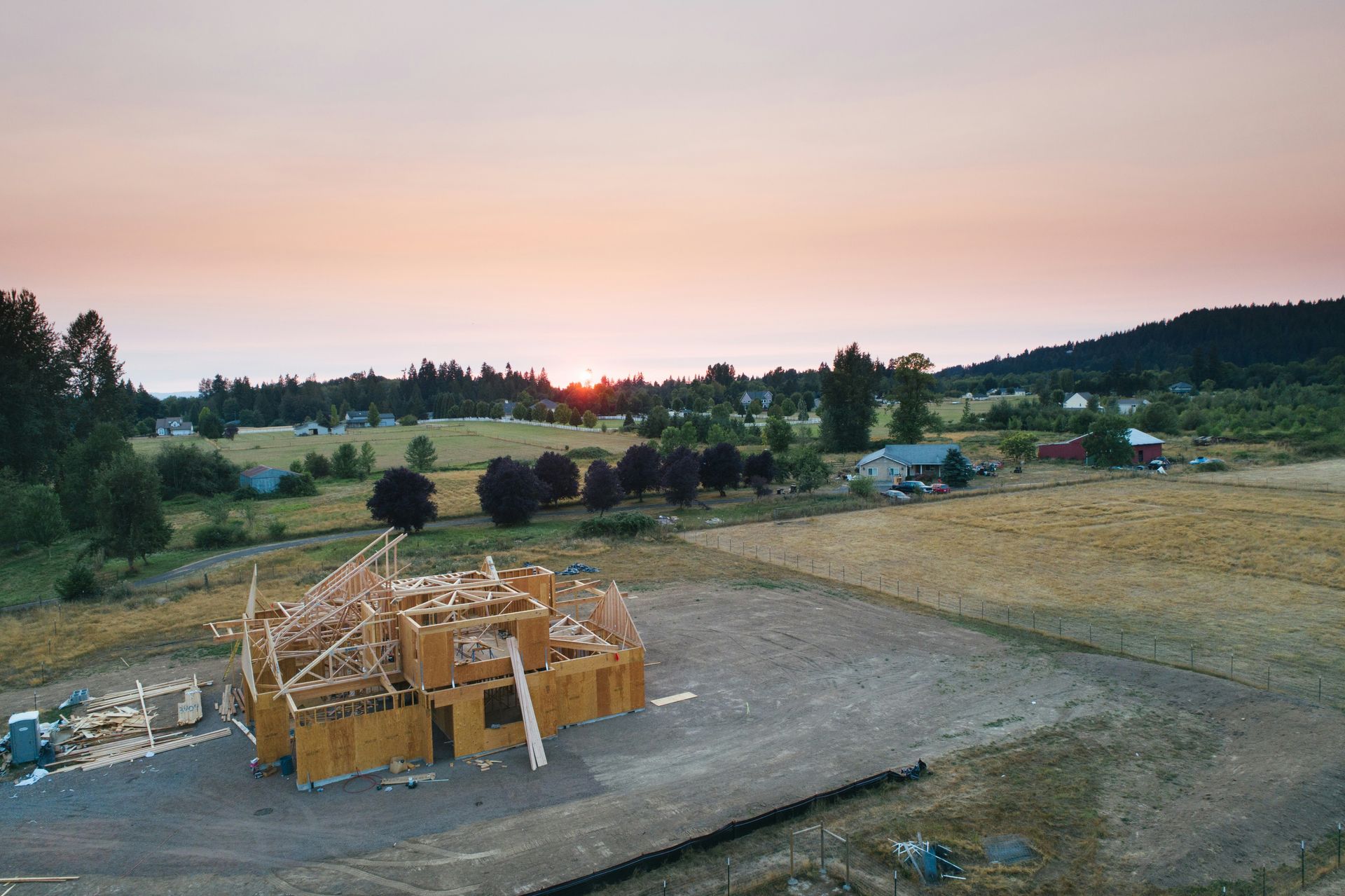 An aerial view of a house under construction in a field at sunset.