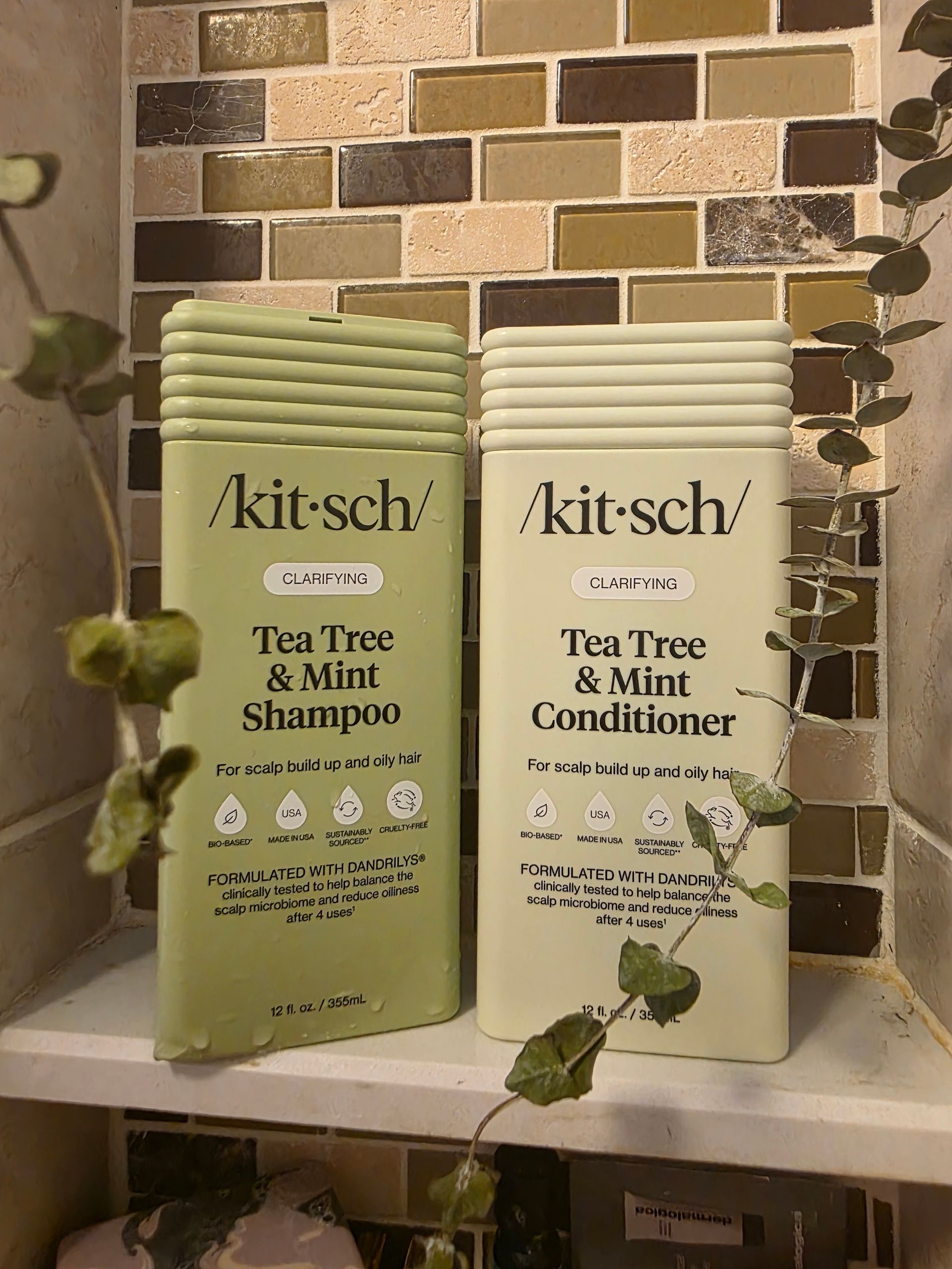 Two kitsch Tea Tree & Mint hair products, green shampoo and white conditioner, on a tiled shelf.