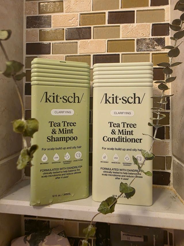 Two Kit-sch Tea Tree & Mint shampoo and conditioner bottles on a tiled counter with greenery.