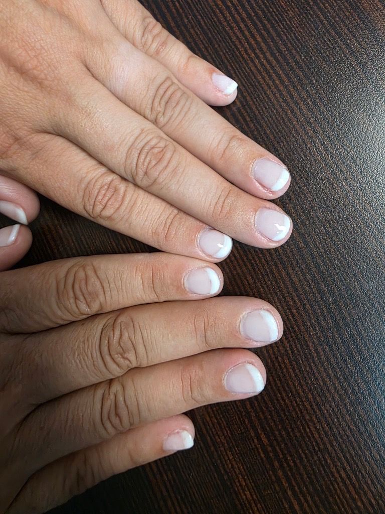 Two hands with short French manicure nails on a dark textured surface