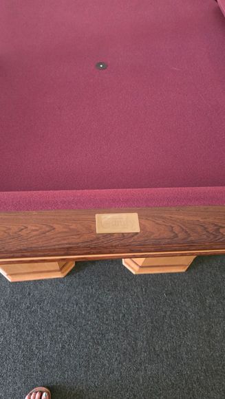 this is A beige pool table with dark wood trim in a game room, beside a red-felt table and windows.