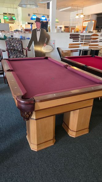 this is A beige pool table with dark wood trim in a game room, beside a red-felt table and windows.