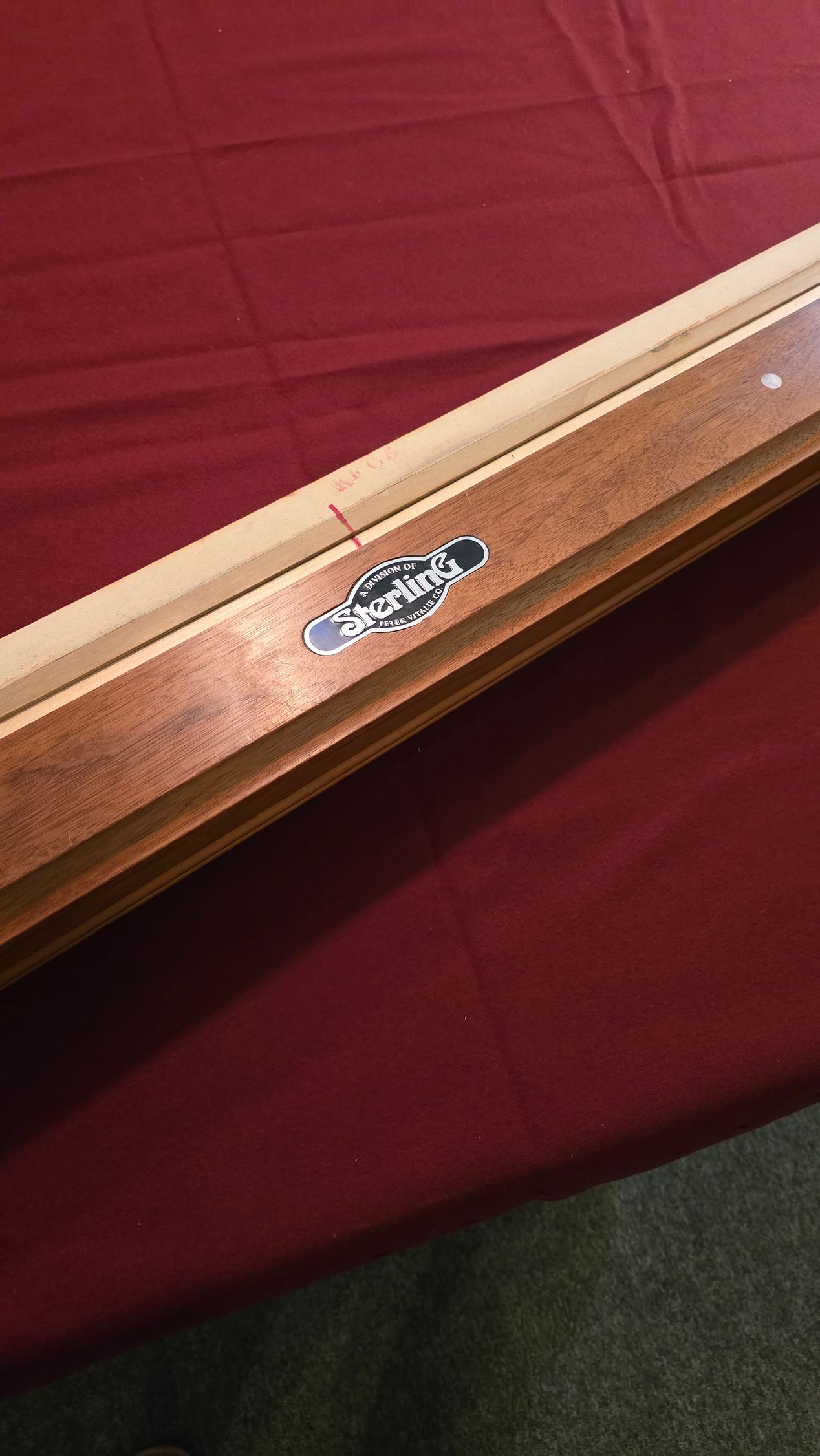 this is A beige pool table with dark wood trim in a game room, beside a red-felt table and windows.
