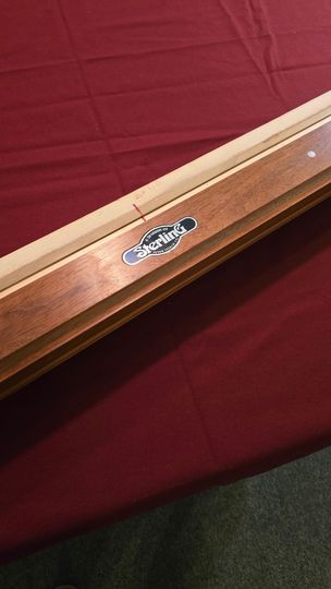 this is A beige pool table with dark wood trim in a game room, beside a red-felt table and windows.