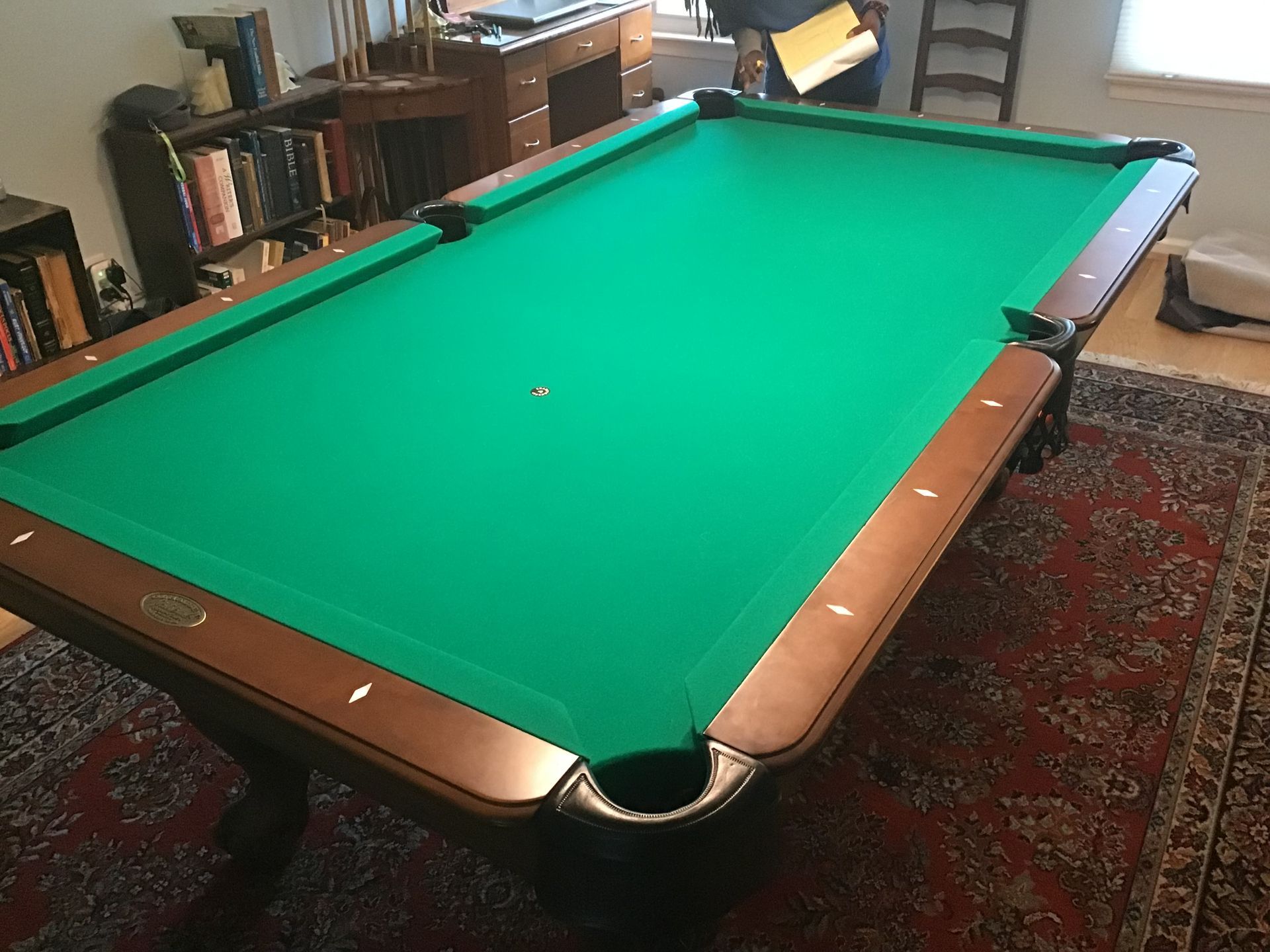 Green pool table in a carpeted room, with wooden rails and a single ball near the center.