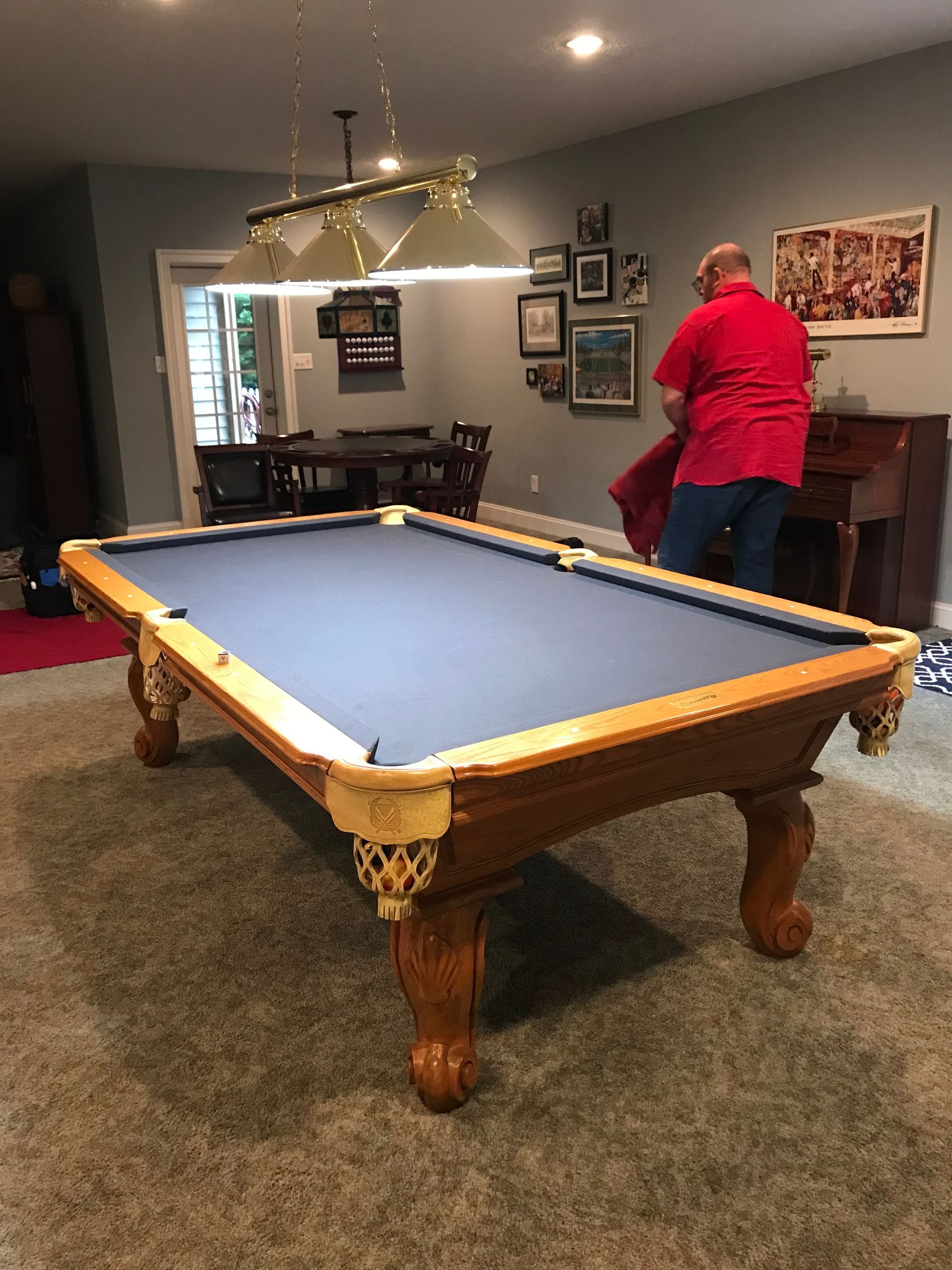 Pool table in a carpeted game room, with a person in a red shirt standing by the wall.